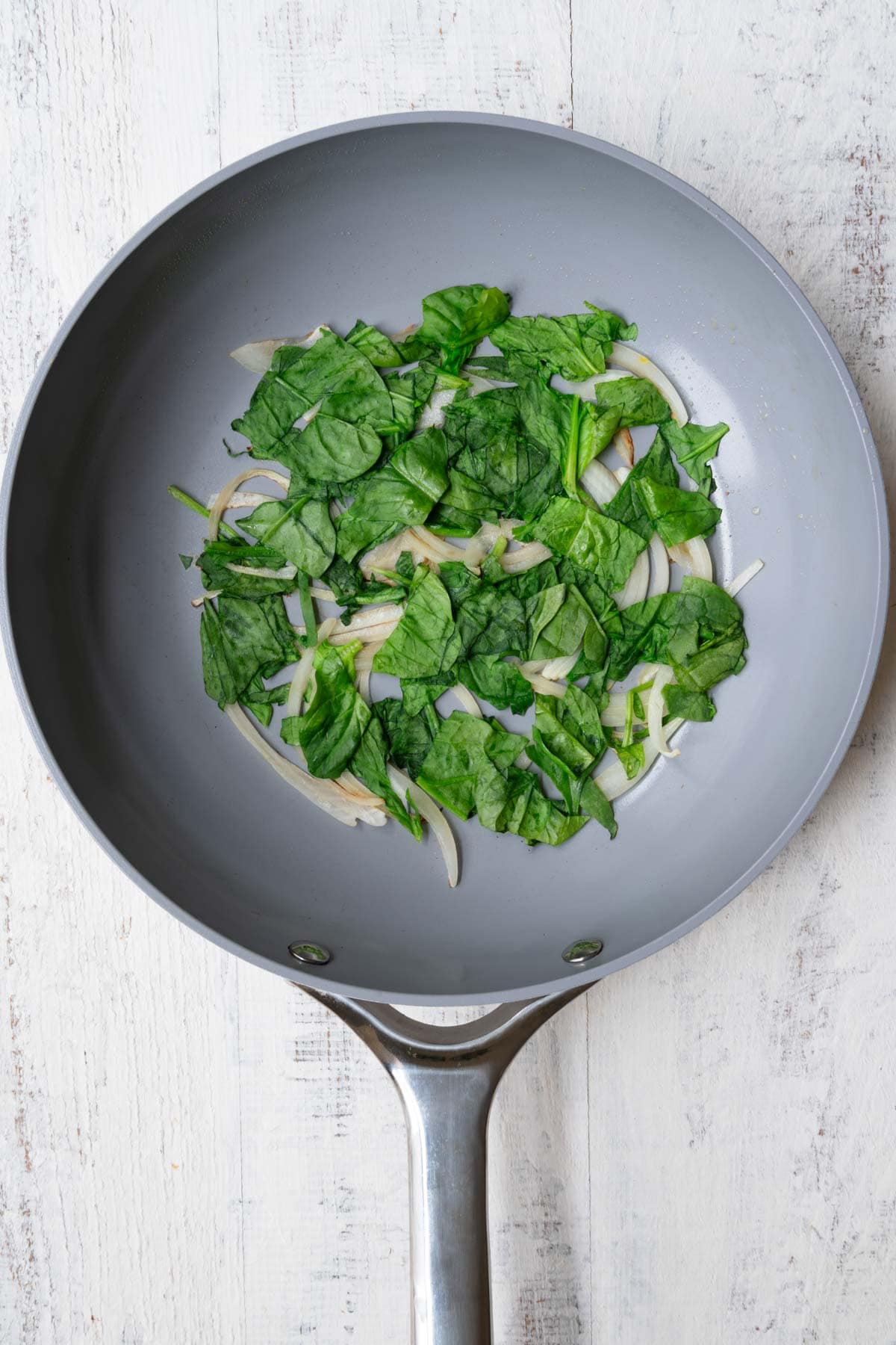 Sliced onion and spinach cooking in a skillet.
