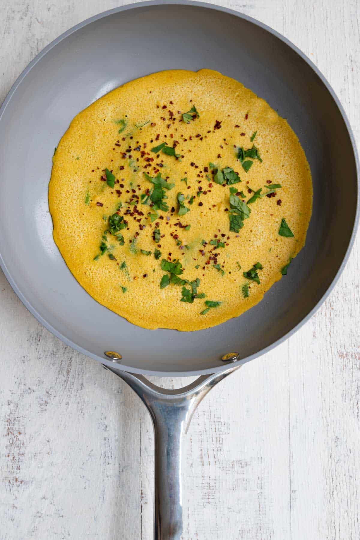 High-protein vegan omelette cooking in a nonstick skillet with chopped herbs.