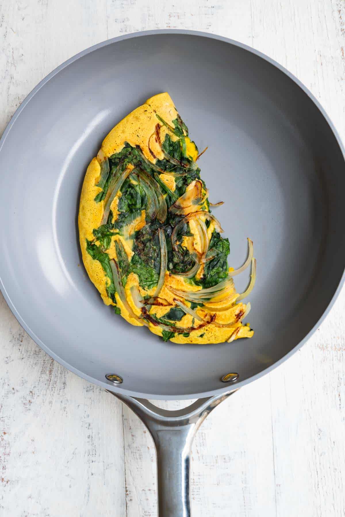 High-protein vegan omelette with onion and spinach in a nonstick skillet.
