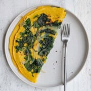 High-protein vegan omelette with onion and spinach on a white plate with a fork.