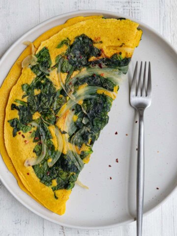 High-protein vegan omelette with onion and spinach on a white plate with a fork.