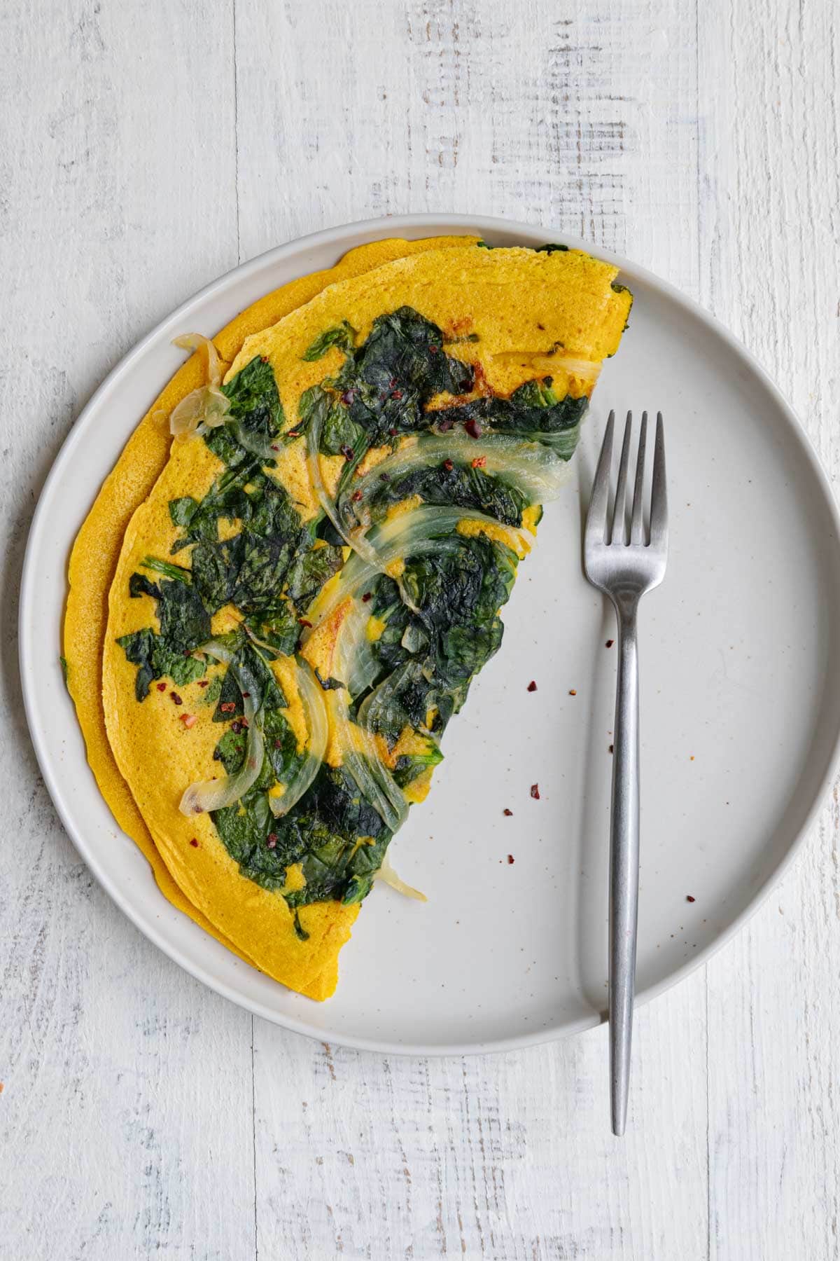 High-protein vegan omelette with onion and spinach on a white plate with a fork.