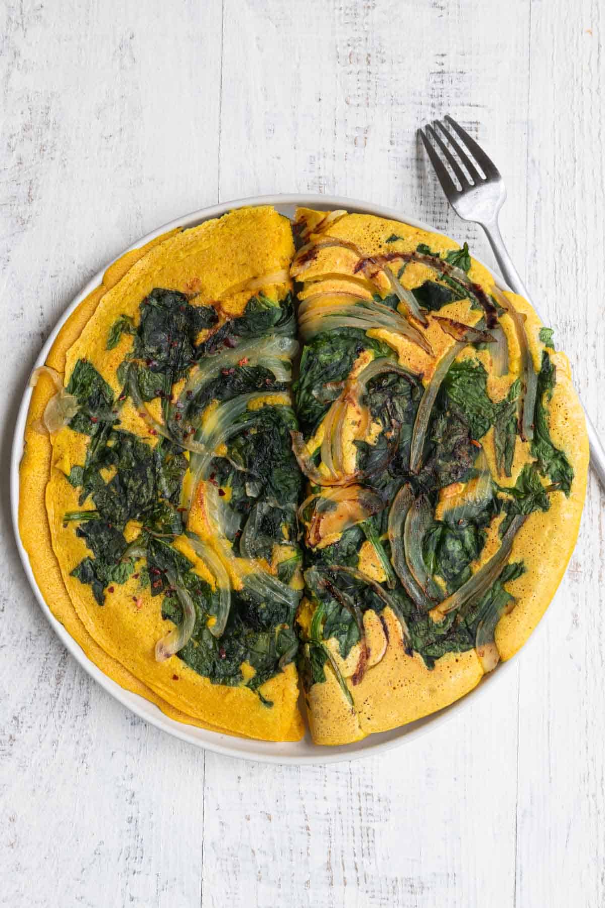 Two vegan omelettes with spinach and onion on a white plate.