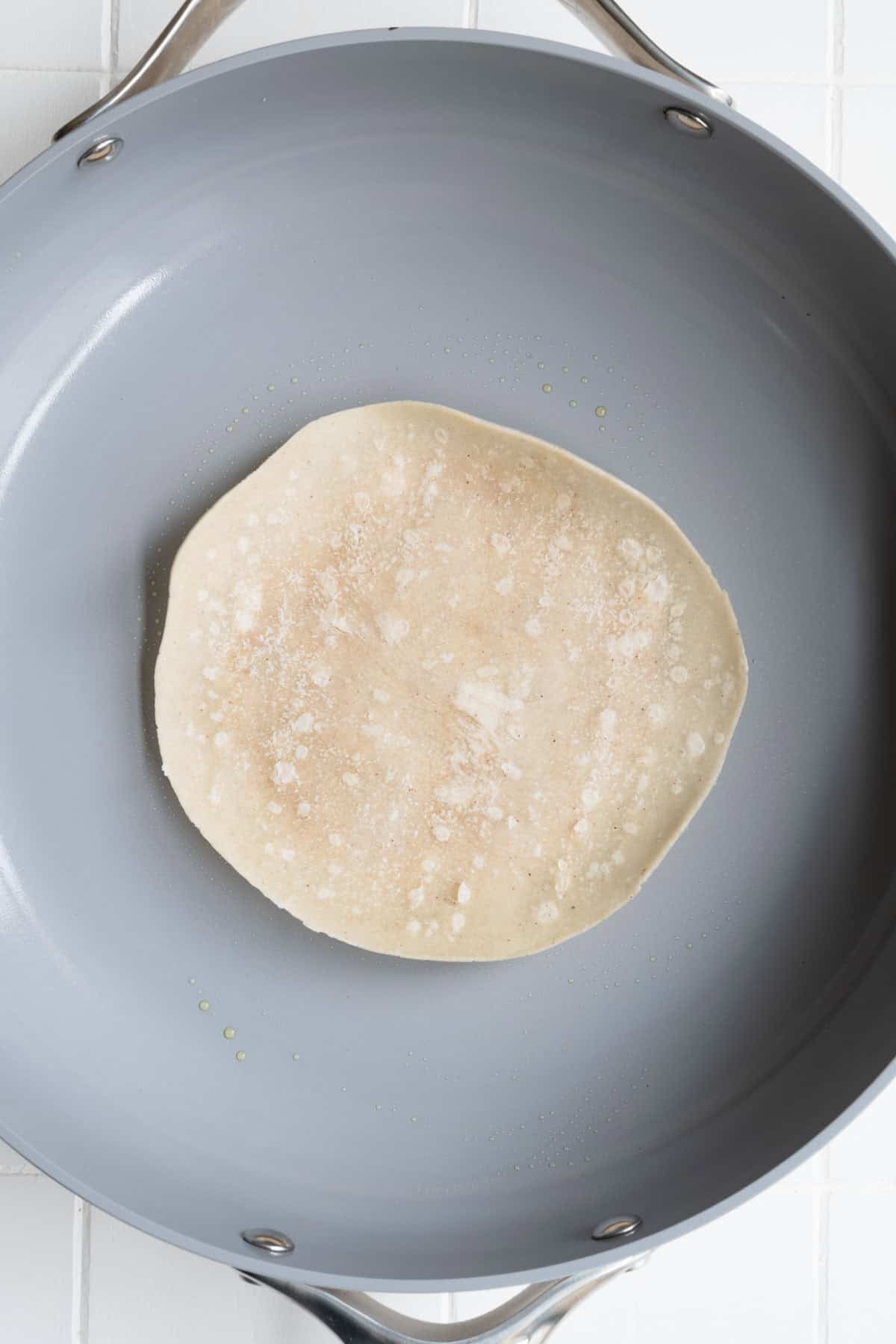 Vegan smash burger with a tortilla on top in a nonstick skillet.