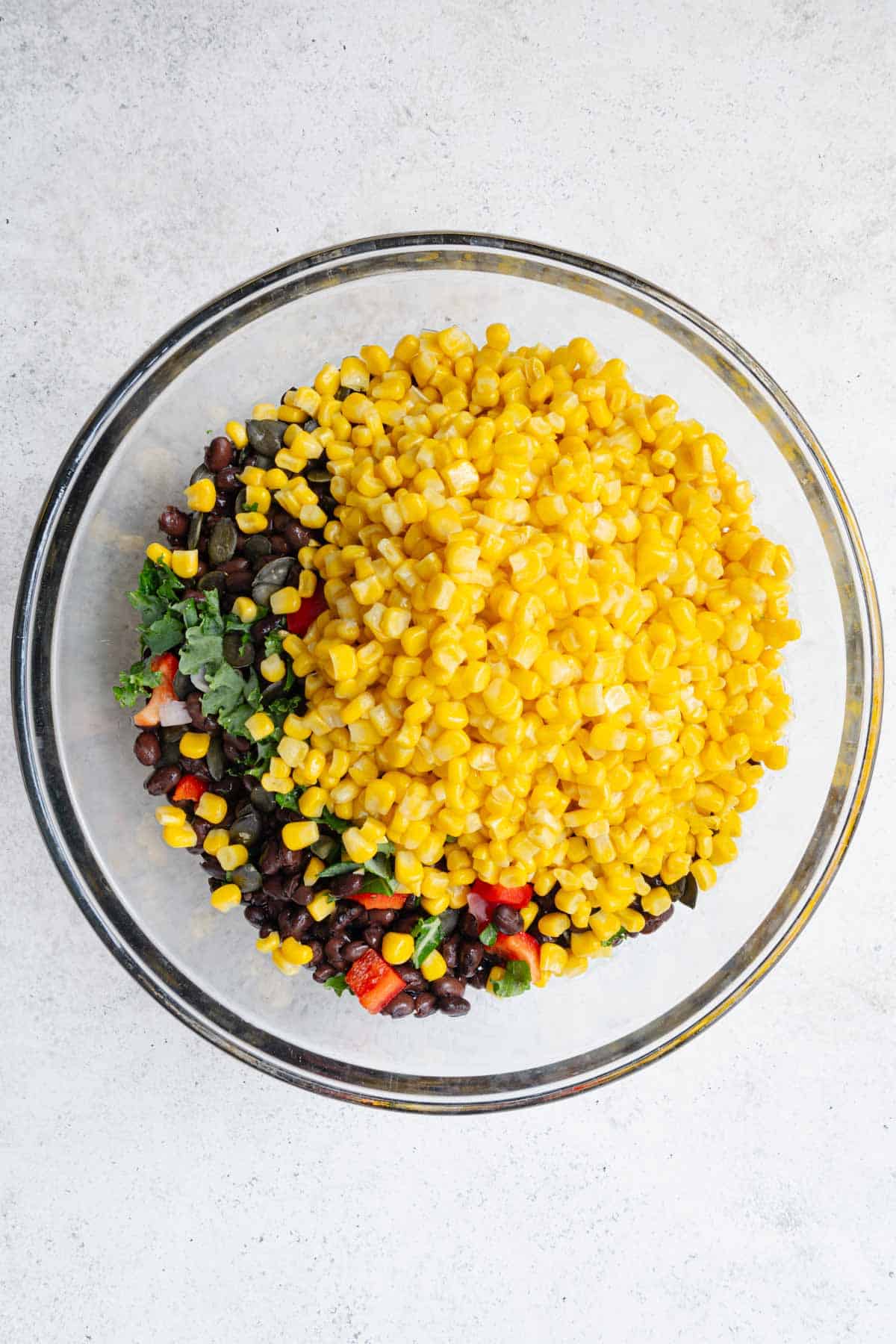 Black bean, corn, and chopped kale, shallot, and red bell peppers in a large glass bowl.