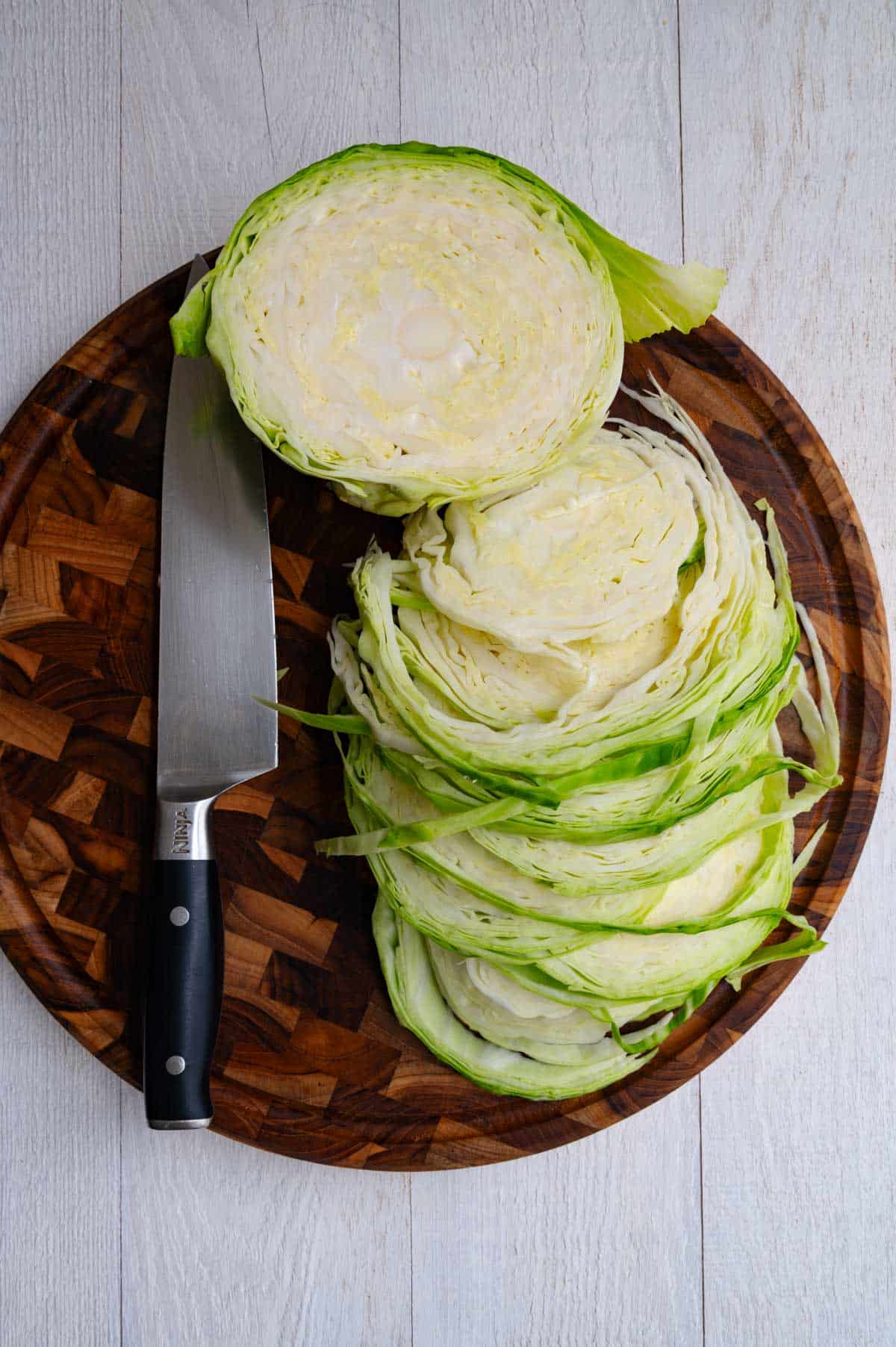 Sliced cabbage on a wooden cutting board with a knife.