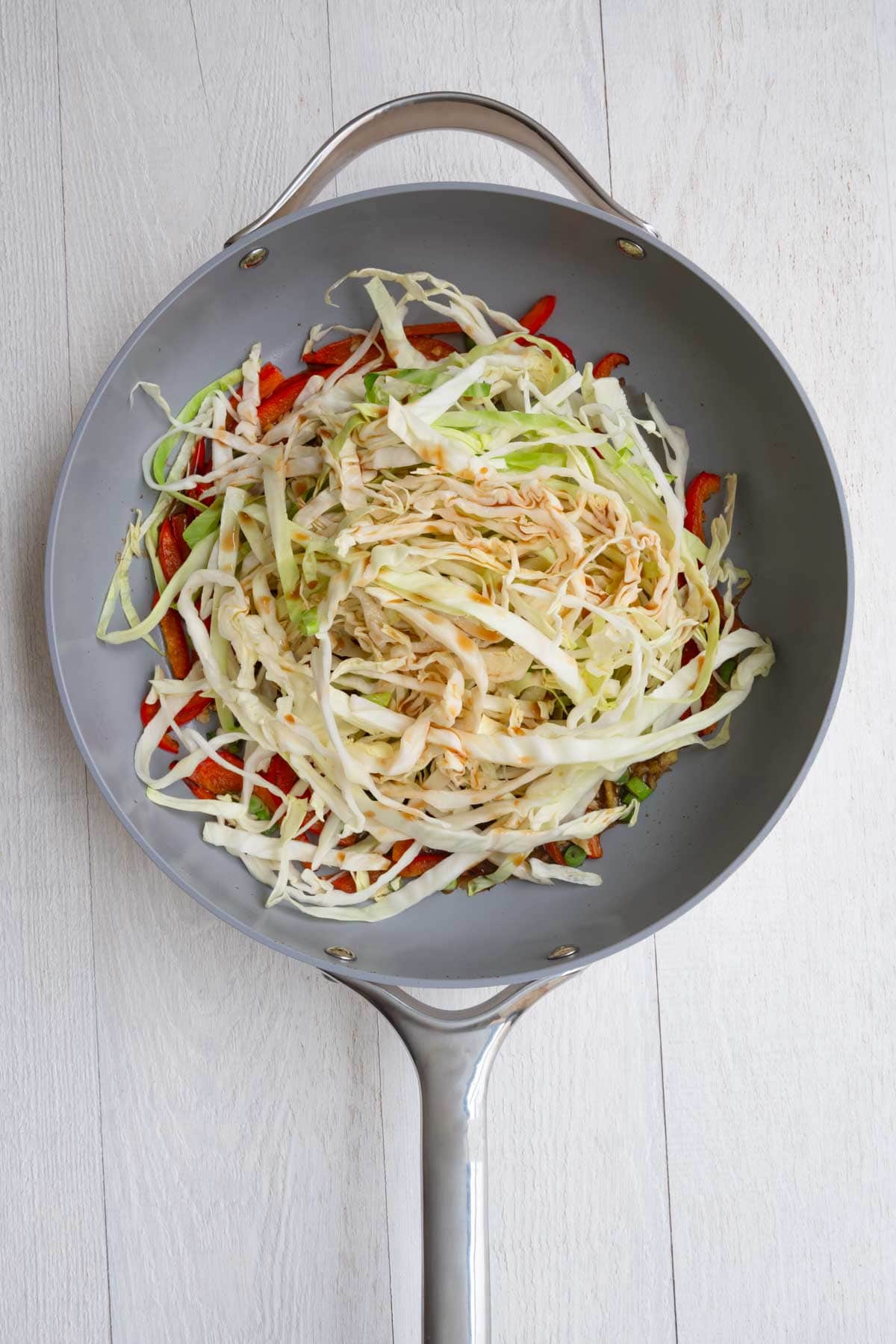 Cabbage, bell pepper, stir-fry sauce, garlic, green onion, and ginger cooking in a skillet.
