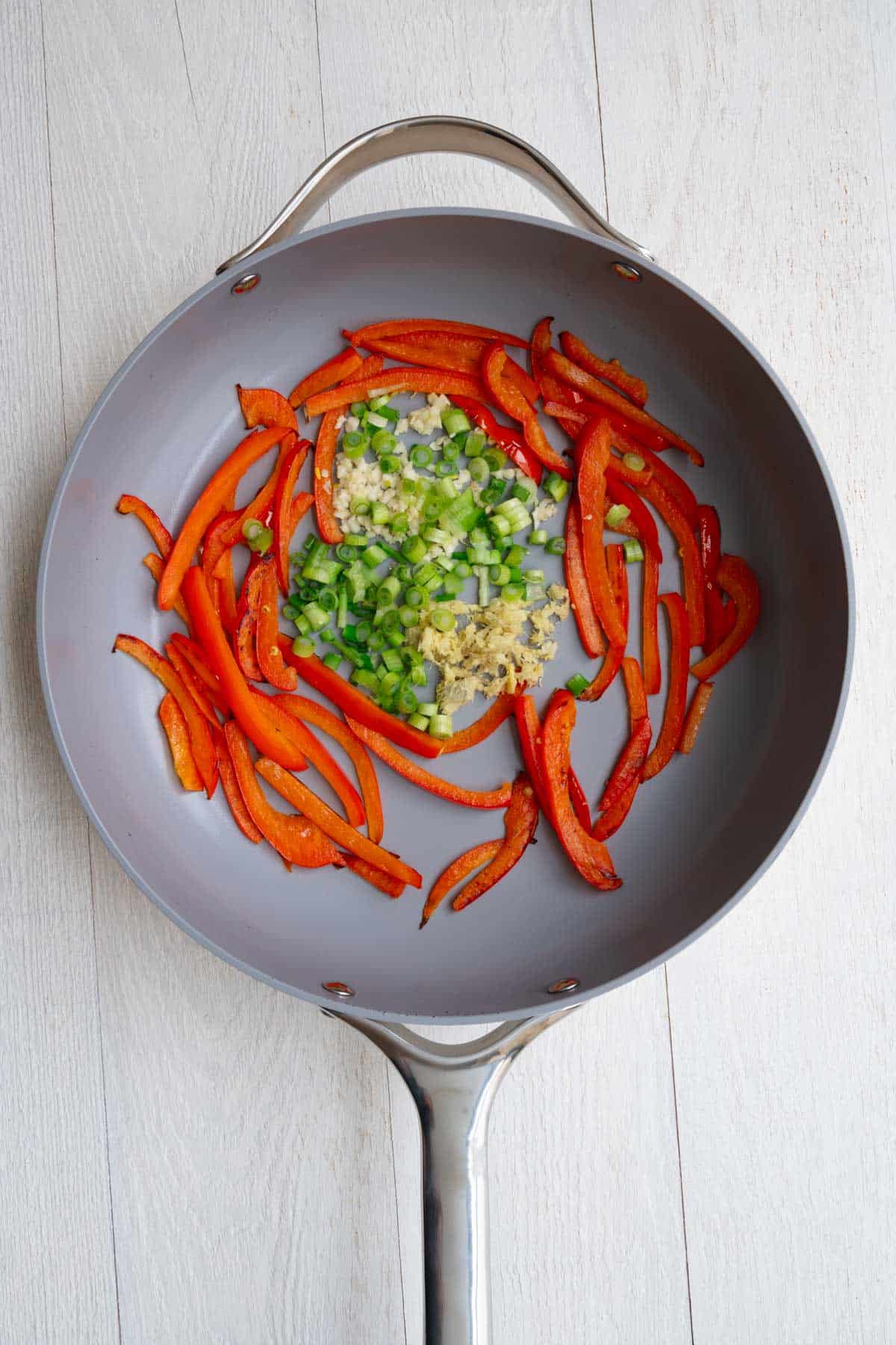 Sautéd red bell peppers in a skillet with garlic, ginger, and sliced green onion.