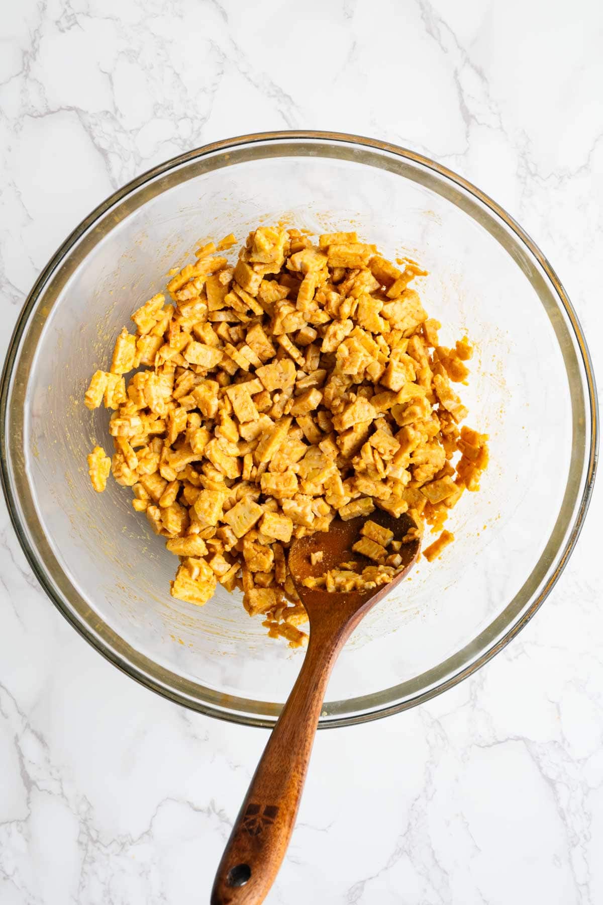 Chopped tempeh tossed with seasonings in a glass bowl.
