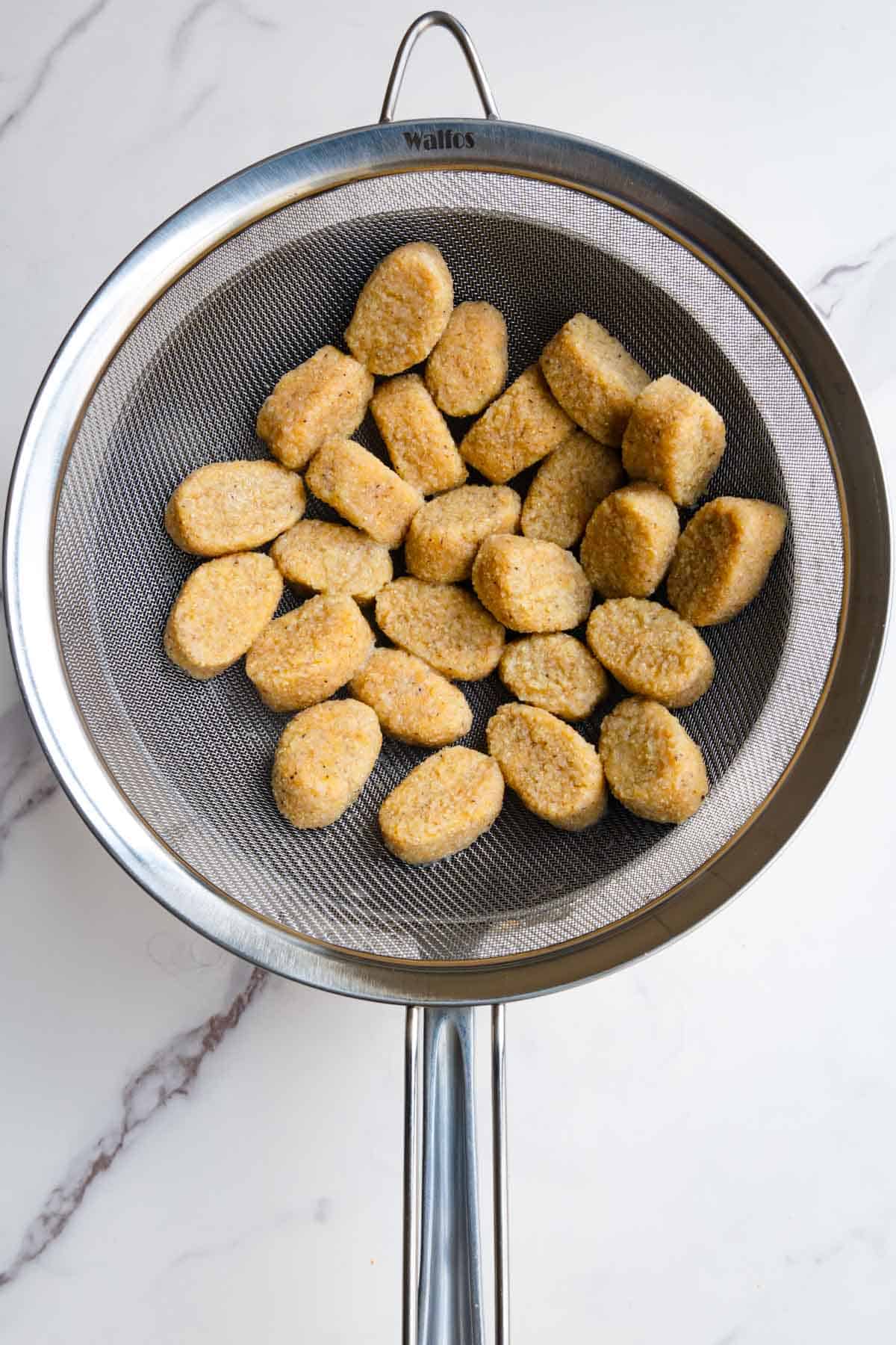 Homemade gnocchi in a fine mesh sieve.