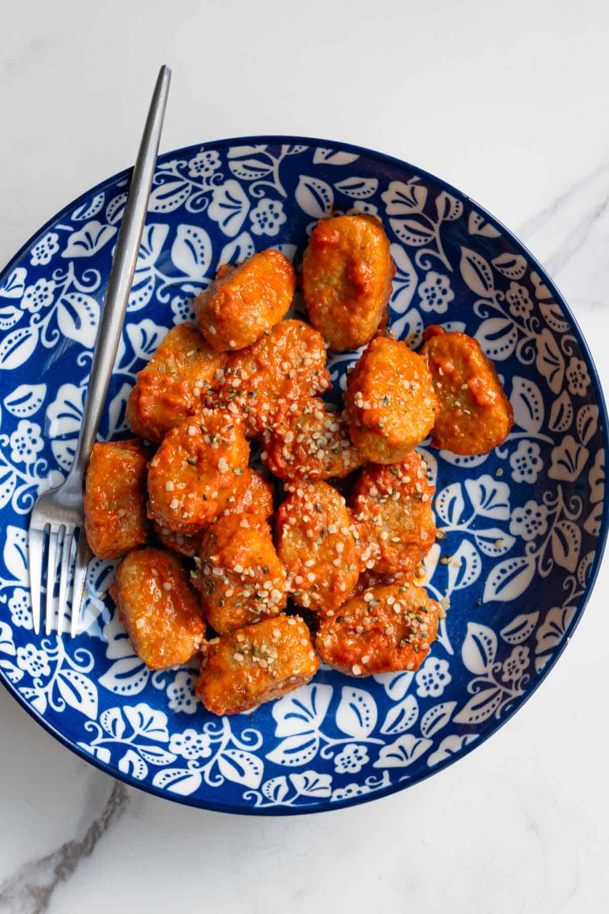 Homemade gnocchi with tomato sauce and hemp hearts in a blue and white bowl.