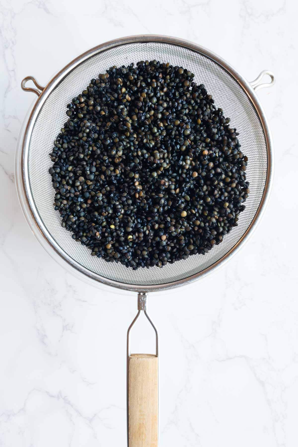 Soaked and drained lentils in a fine mesh sieve.
