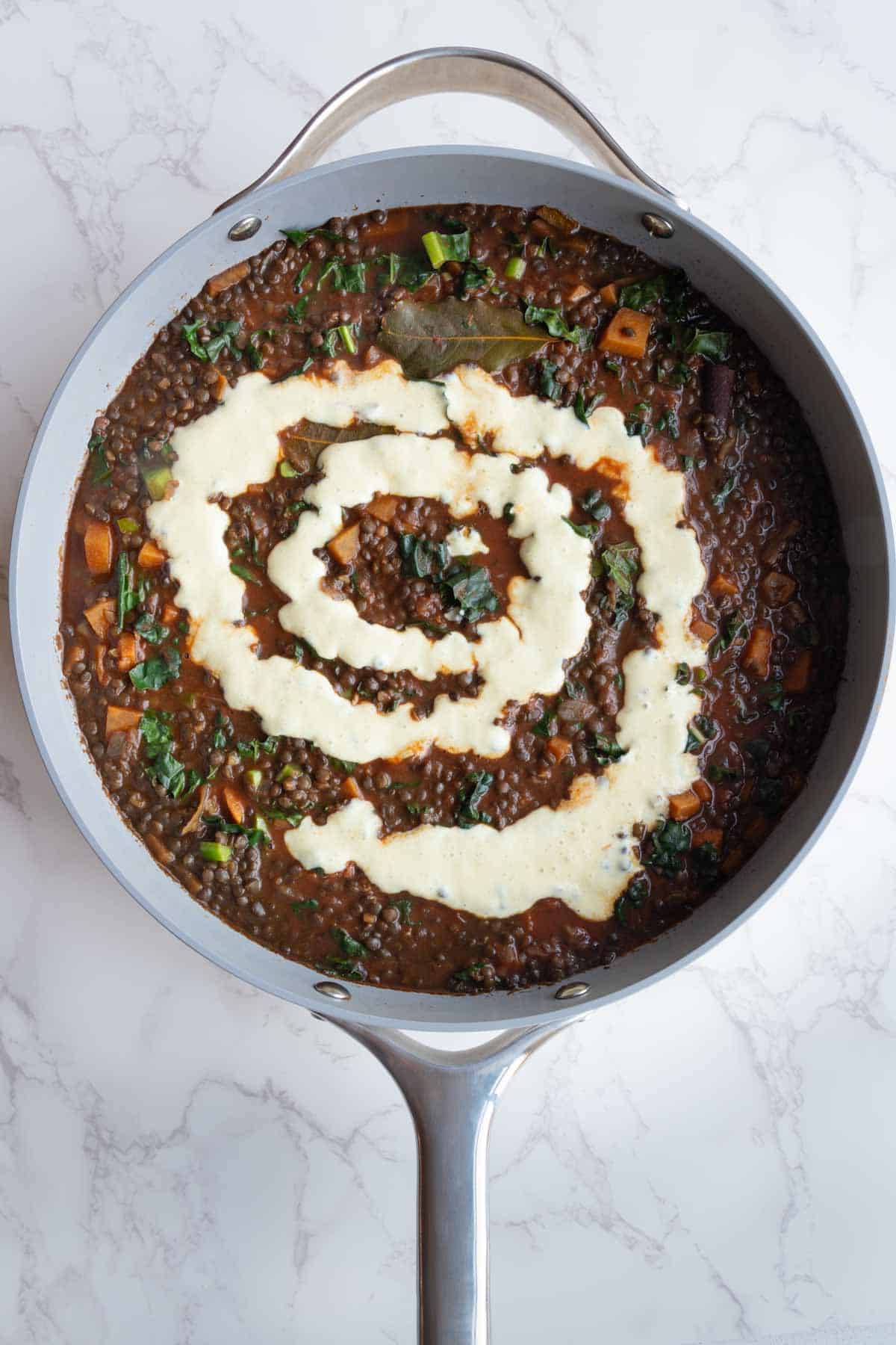 Lentils, greens, and sweet potato cooked in broth and tomato sauce with seasonings and aromatics topped with nondairy cream.
