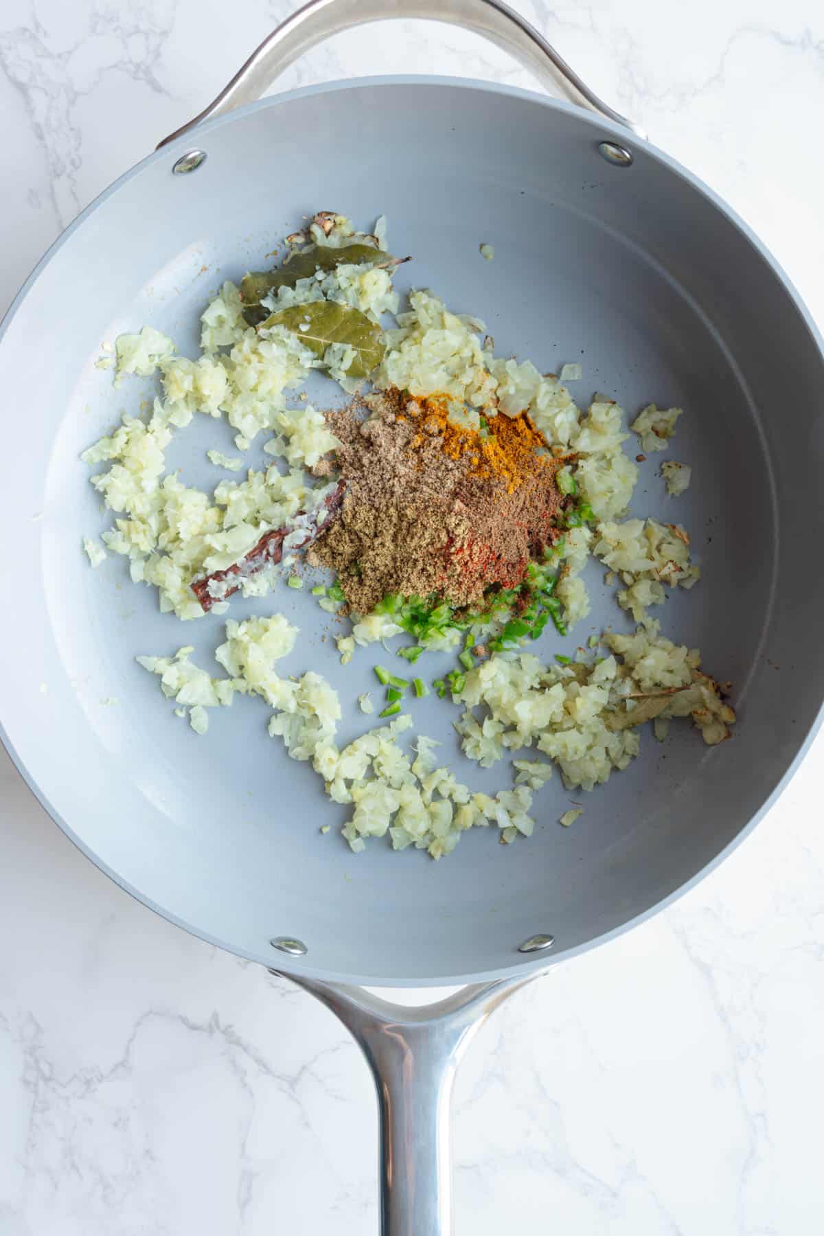 Cooked aromatics with seasonings added in a large skillet.