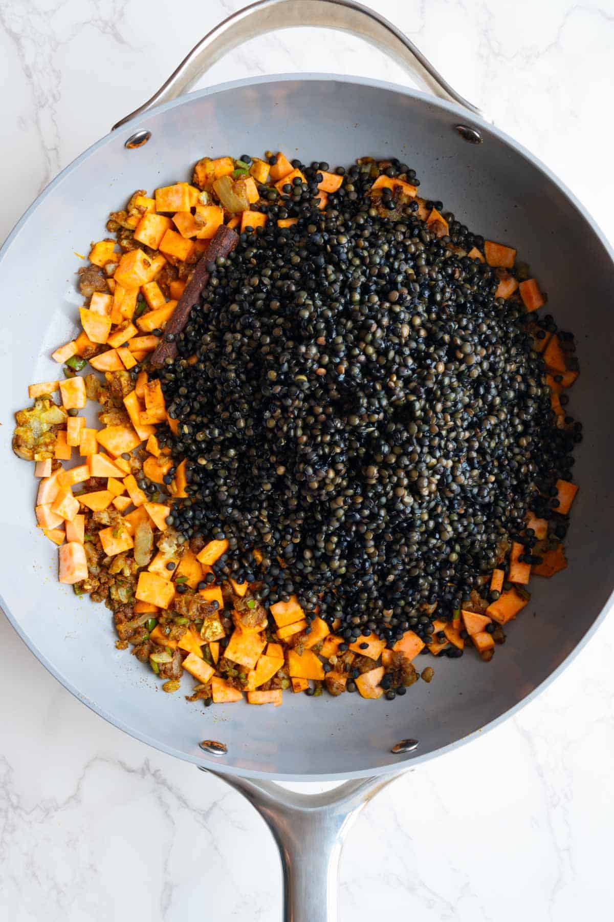 Cooked aromatics and seasonings with chopped sweet potato and black lentils in a large skillet.