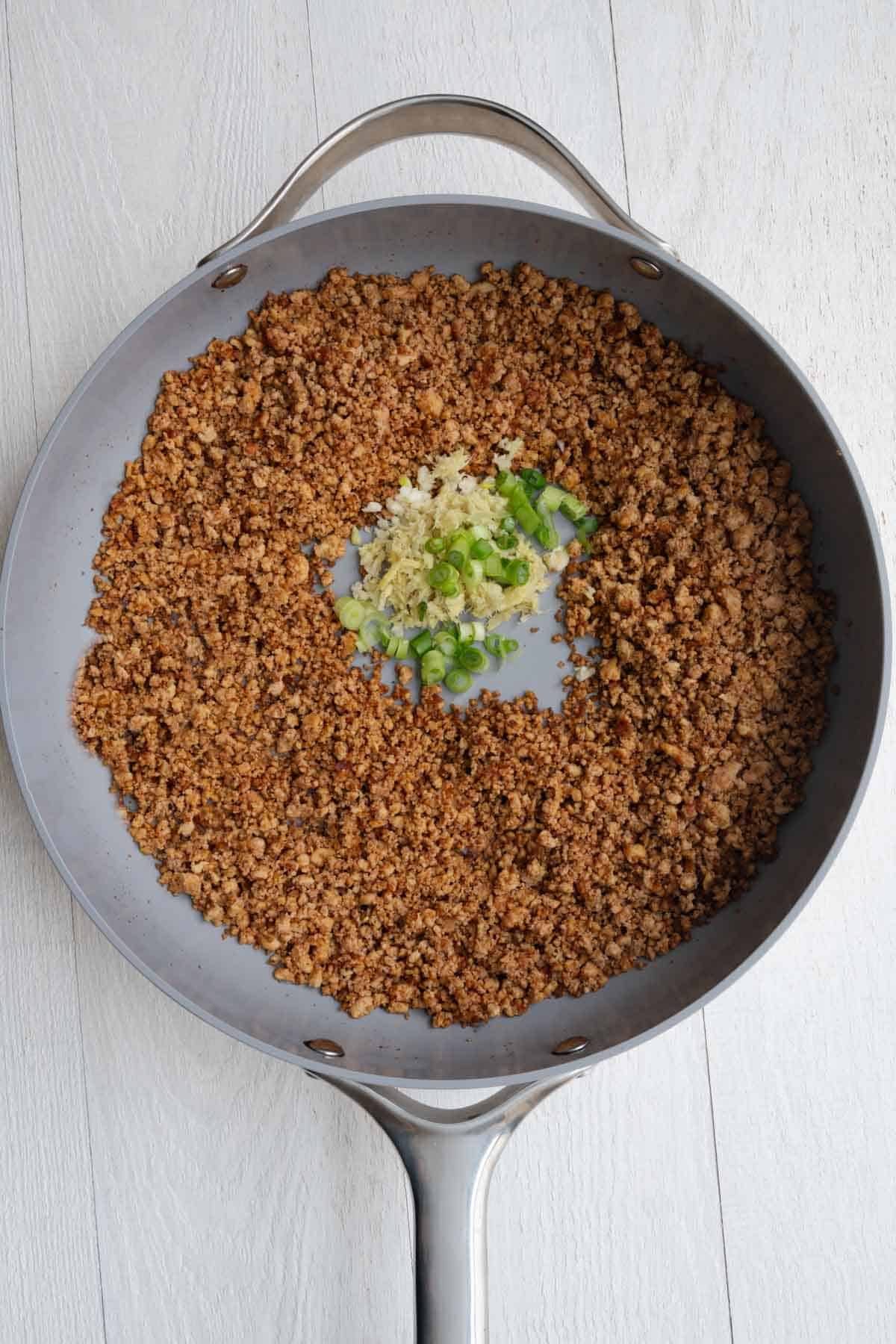 Tofu crumbles browned in a skillet with green onion, garlic, and ginger.