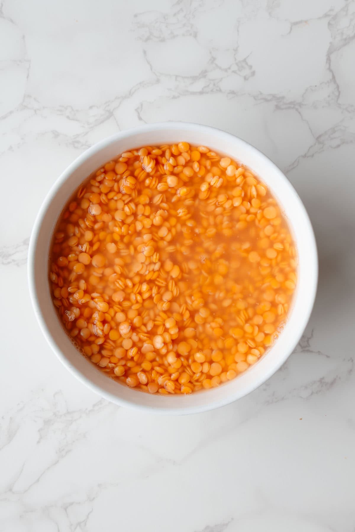 Soaked red lentil in a white bowl.