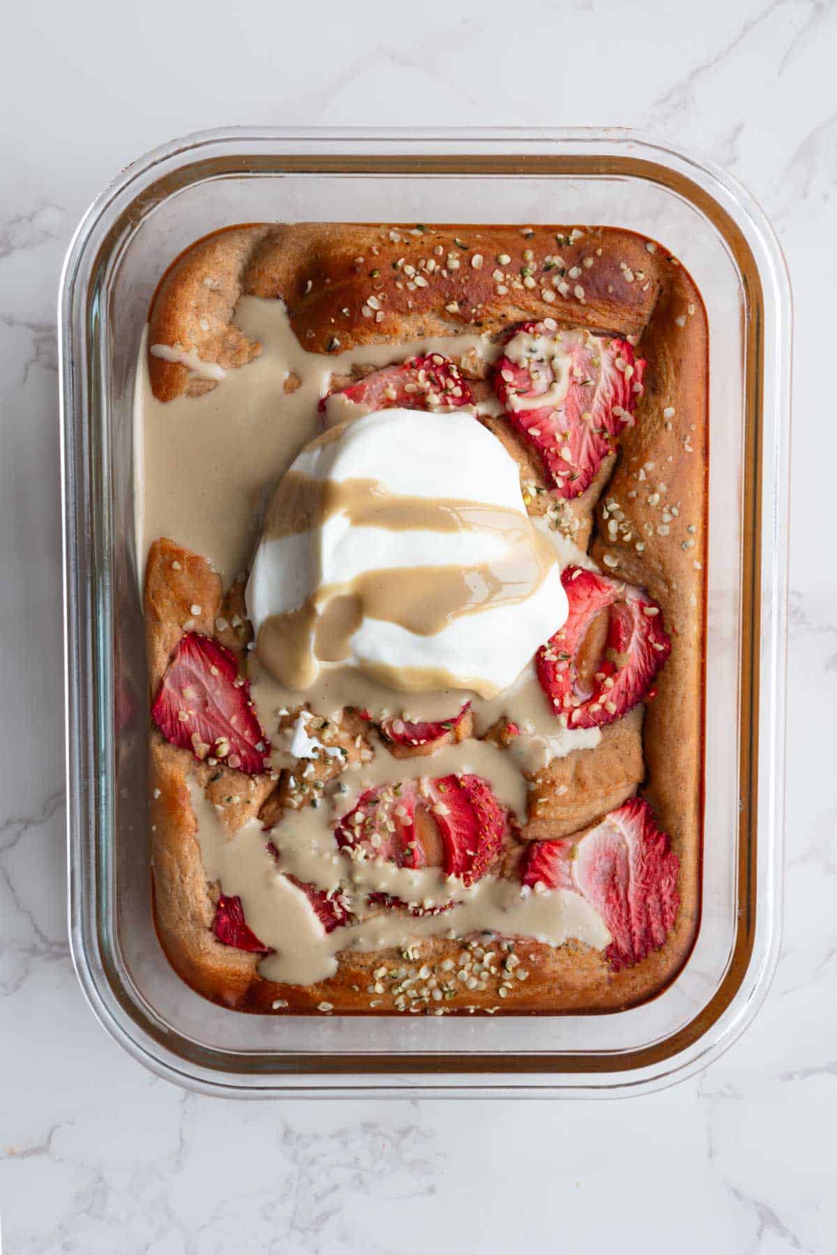 Strawberry hemp heart baked red lentil protein pancake in a glass dish topped with Greek-style yogurt and tahini.