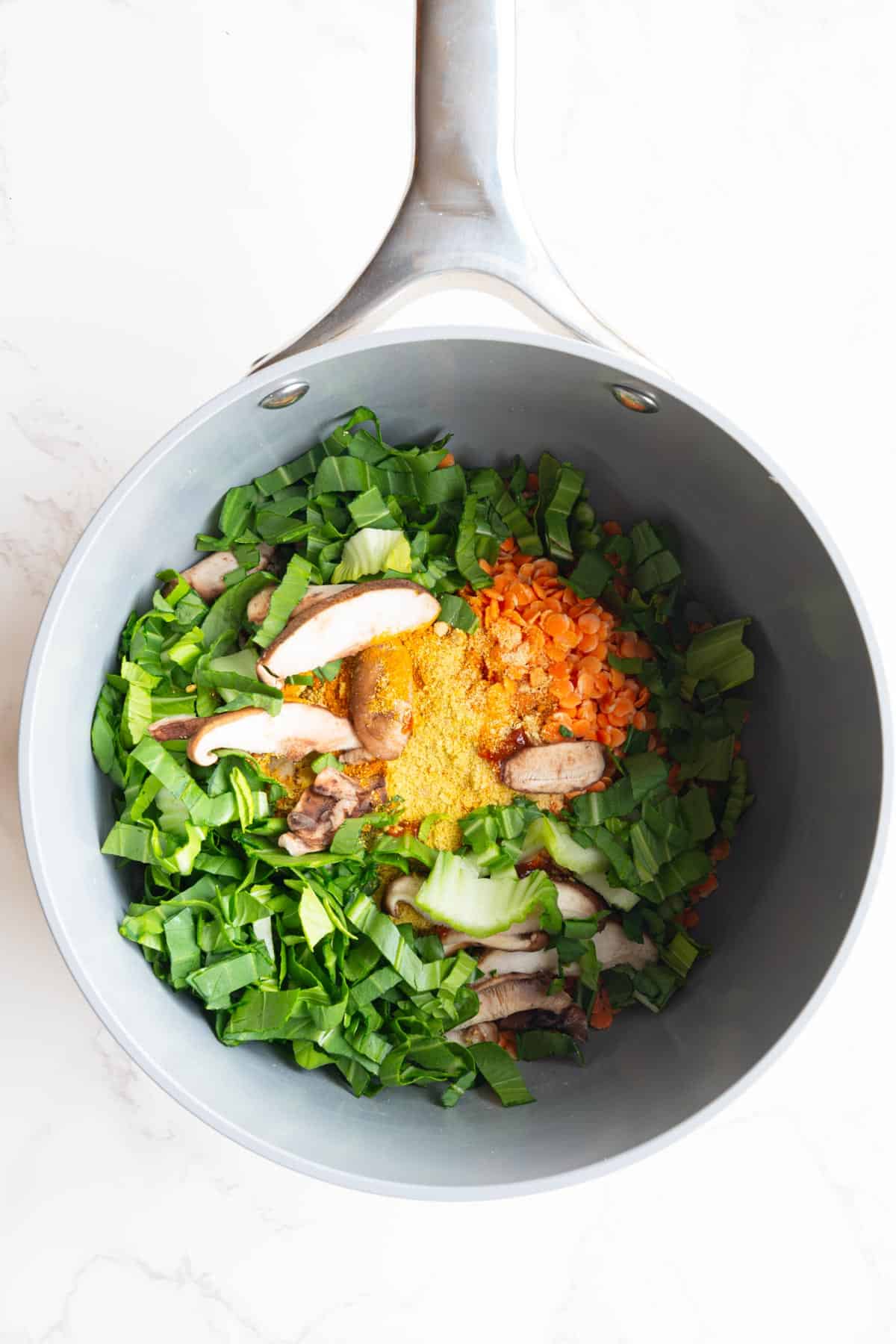 Red lentils, oats, leafy greens, mushrooms, nutritional yeast, and spices in a saucepan.