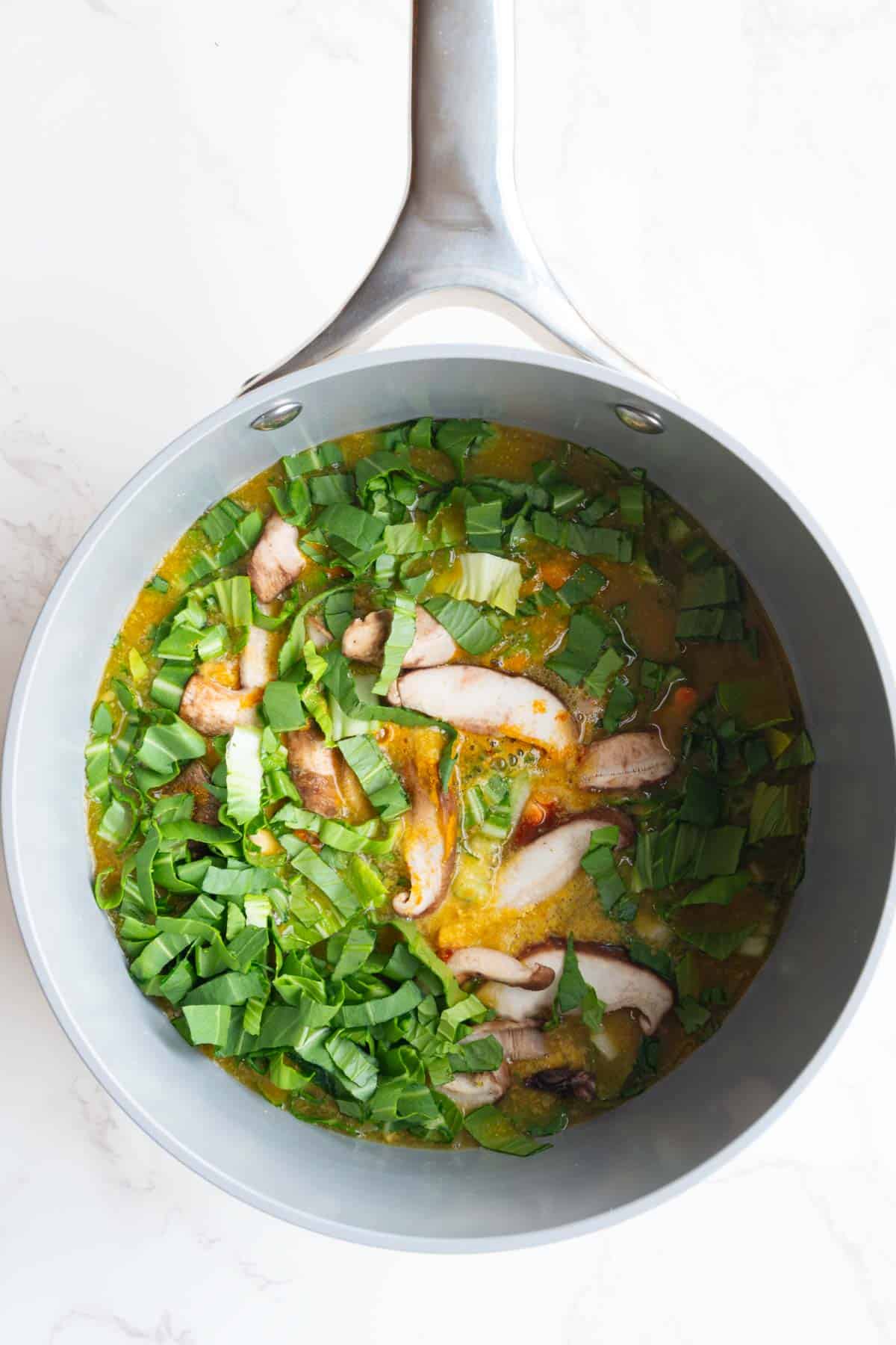 Red lentils, oats, leafy greens, mushrooms, and spices cooking in broth.