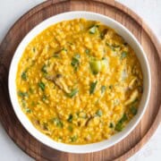 Savory protein porridge with oats and red lentils in a white bowl on a wooden board.