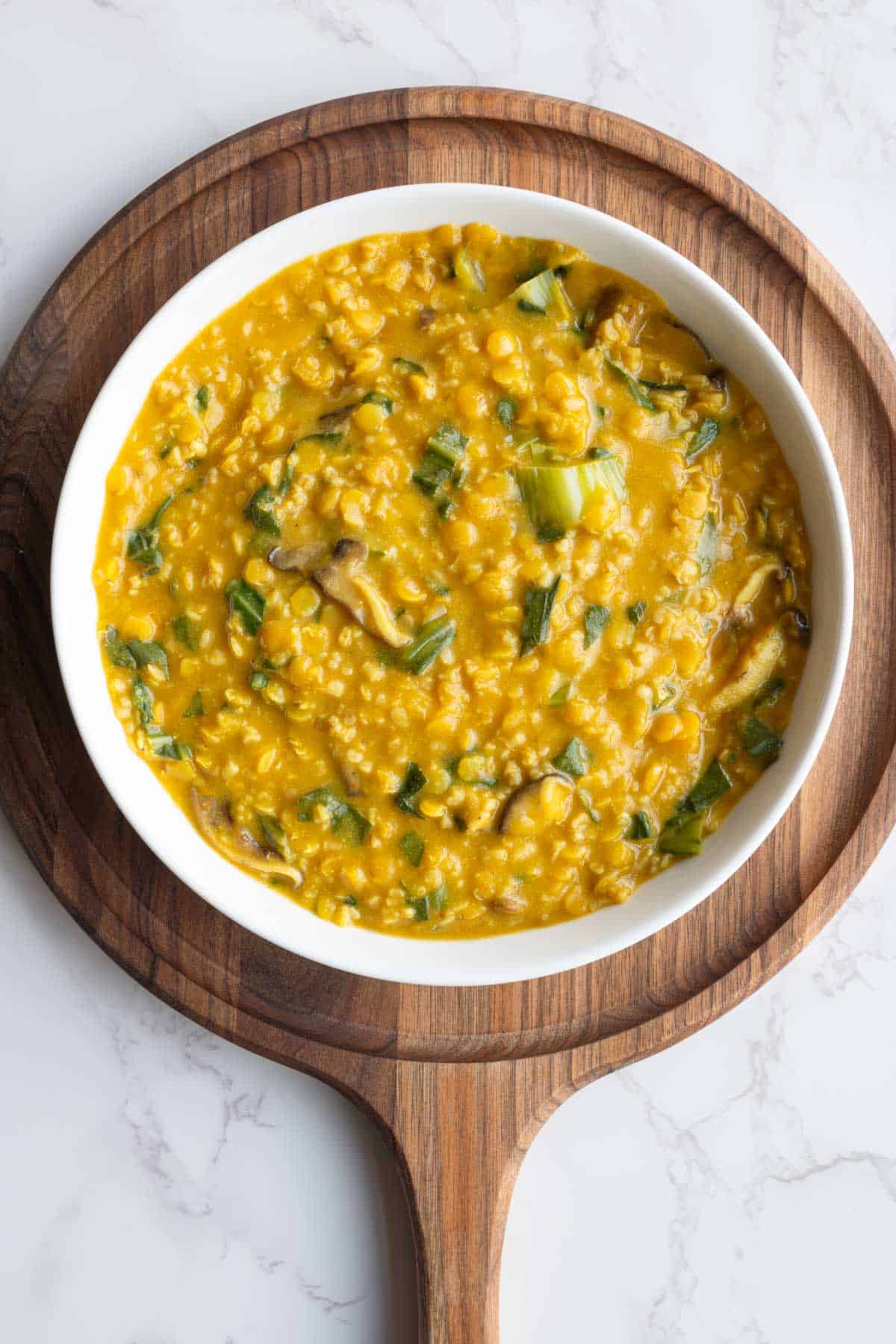 Savory protein porridge with oats and red lentils in a white bowl on a wooden board.