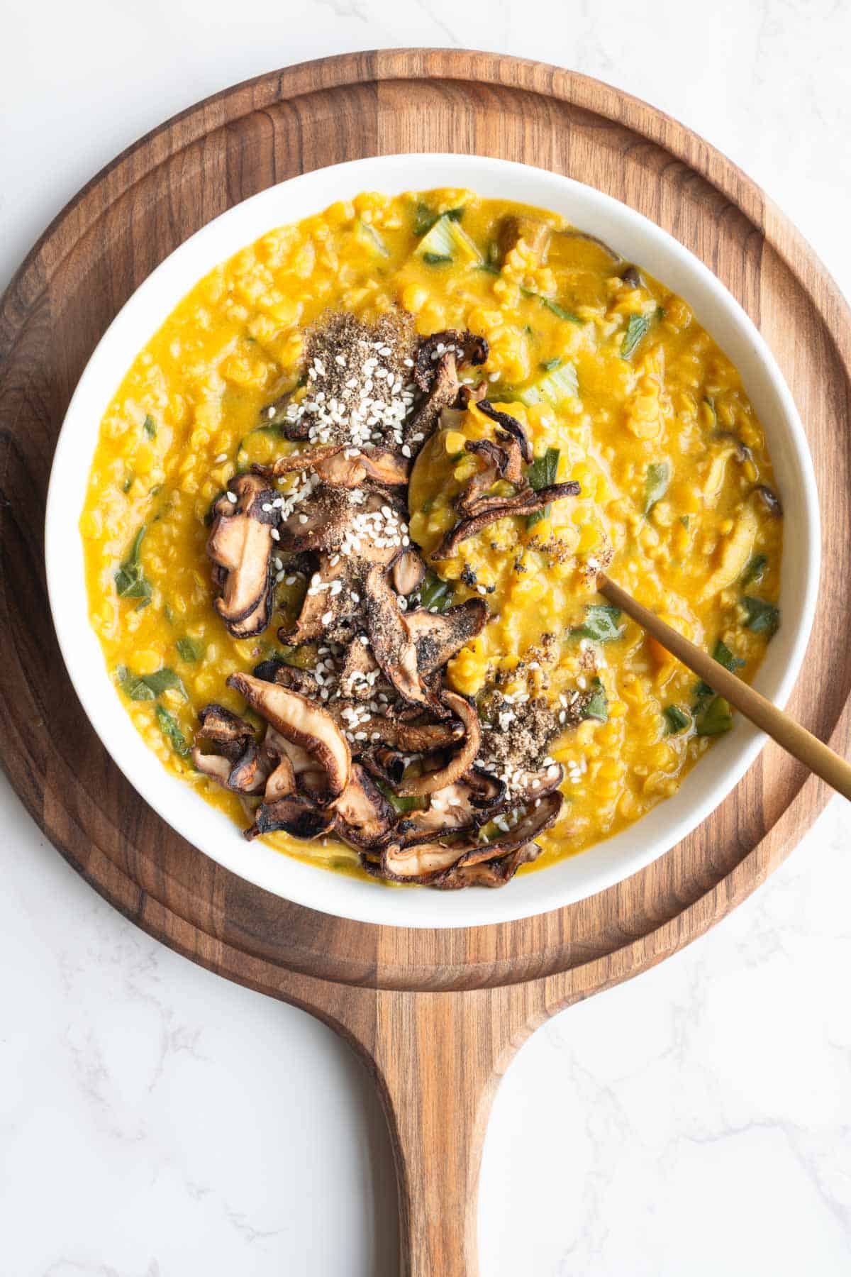Savory protein porridge in a white bowl with a spoon, on a wooden cutting board.