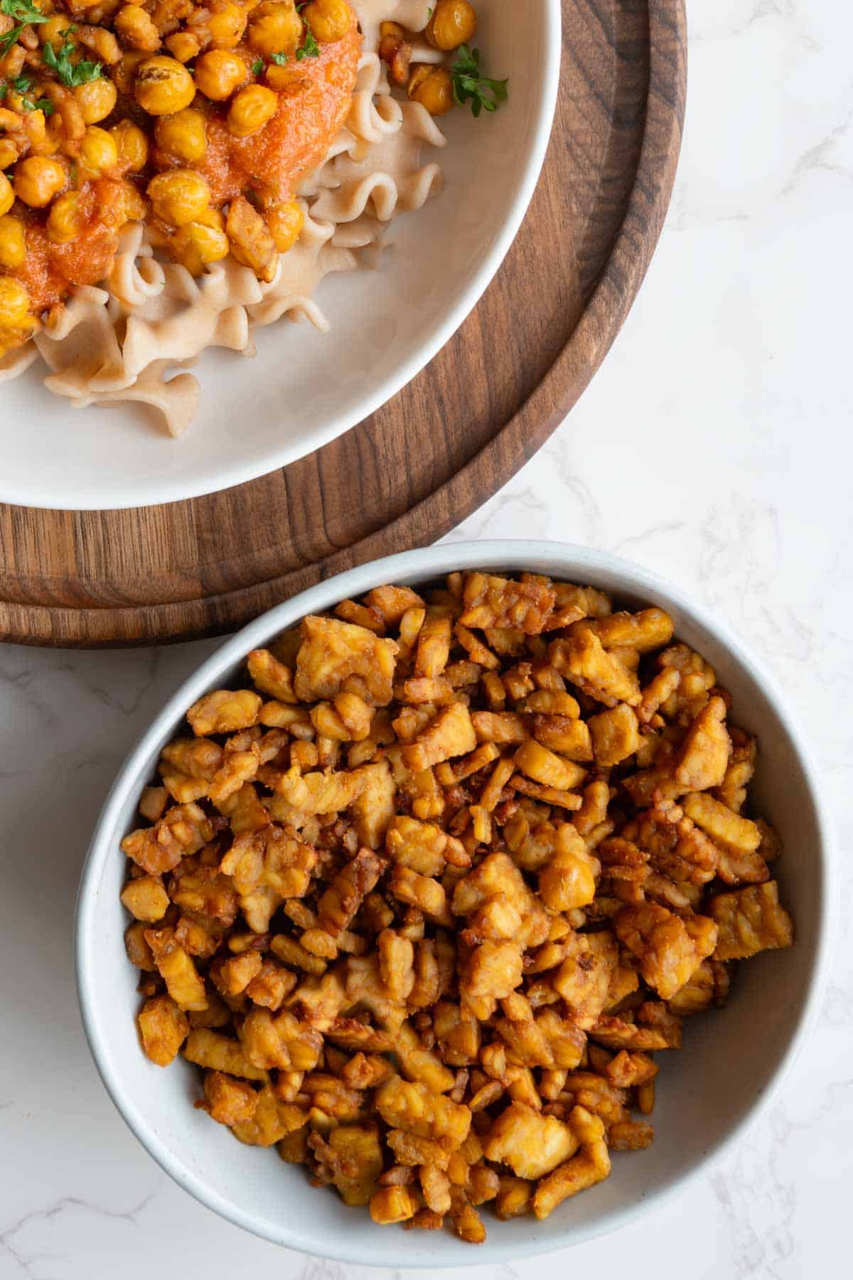 Simple crispy tempeh in a bowl with a pasta tomato sauce dish.