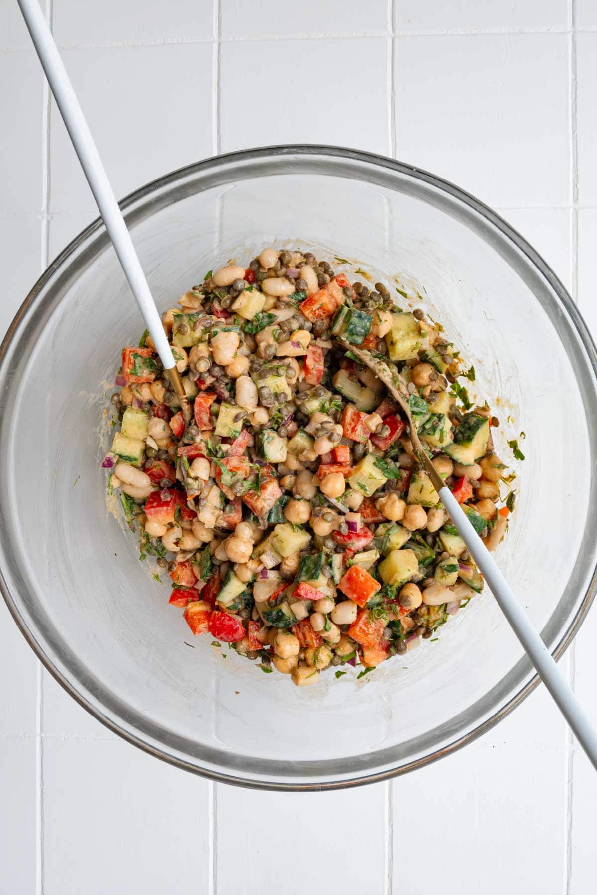 Smoky lemon herb bean salad ingredients in a glass bowl with salad tongs.