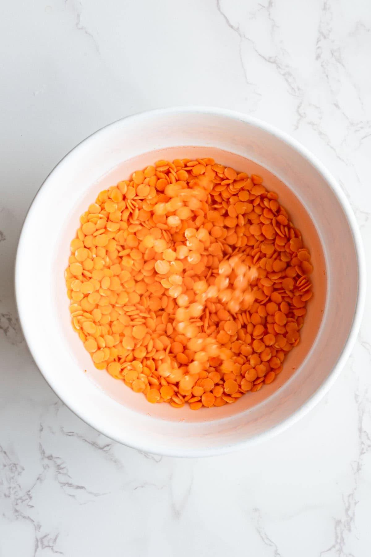 Red lentils soaking in water in a white bowl.
