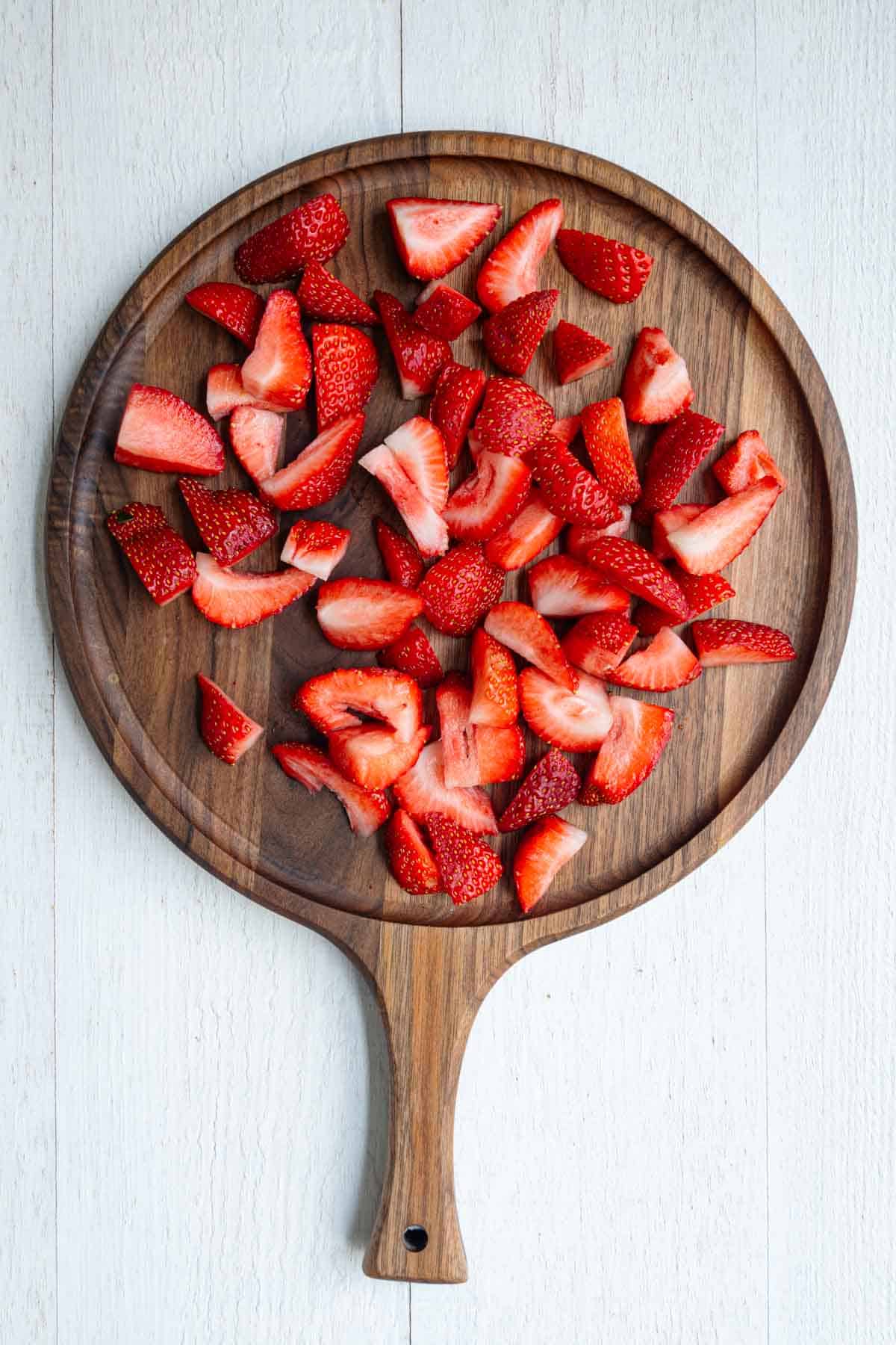 Chopped strawberries on a wooden cutting board.