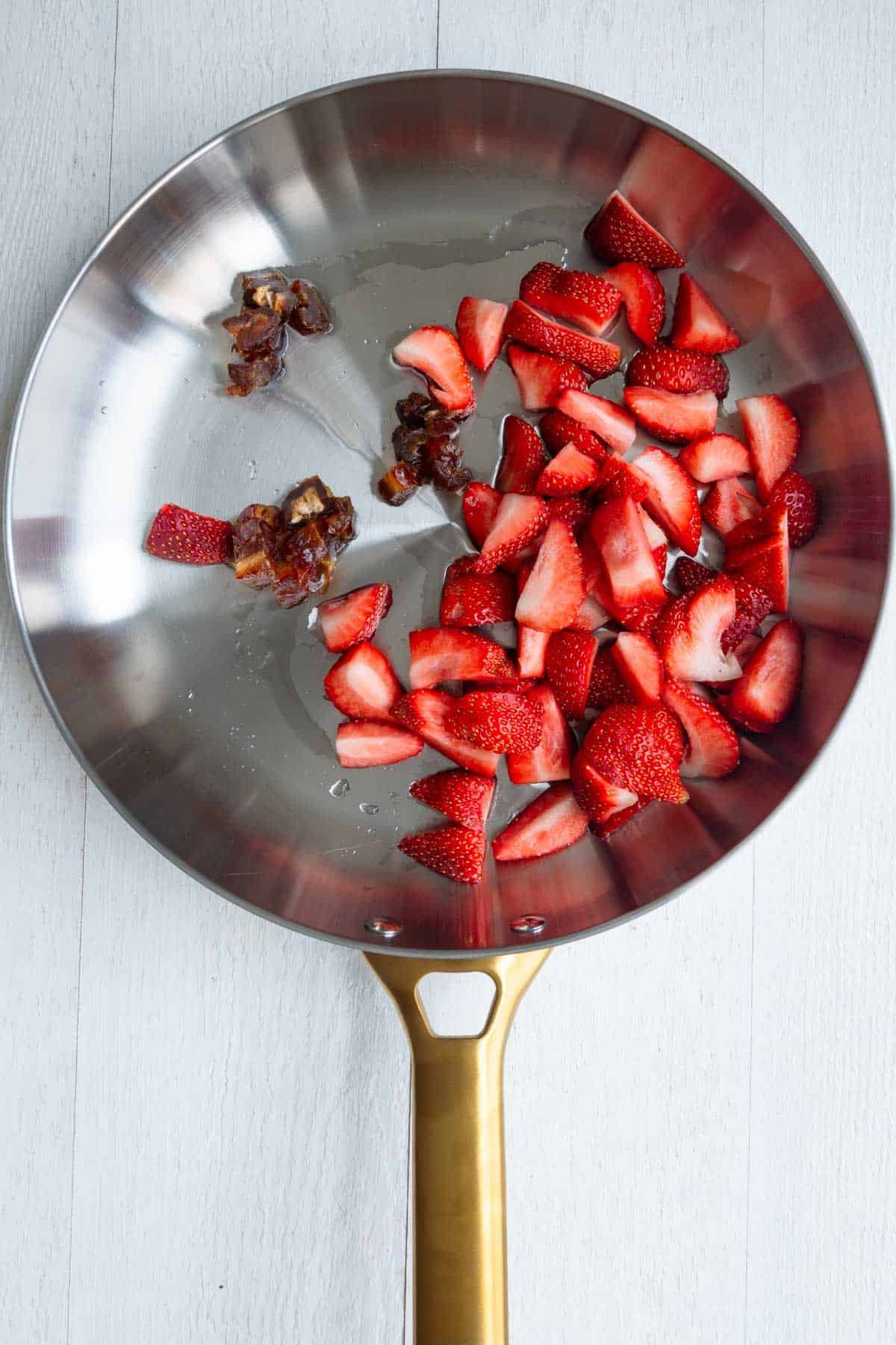 Chopped strawberries and chopped dates in a stainless skillet with a splash of water.