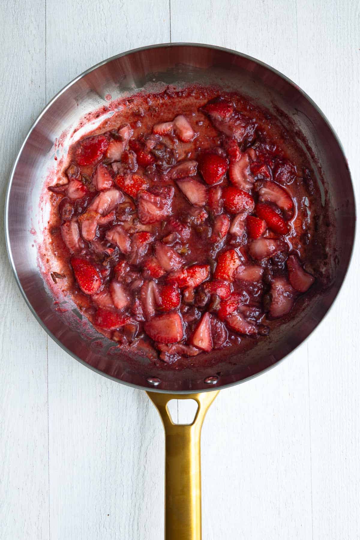 Chopped strawberries and dates cooking in a stainless skillet.