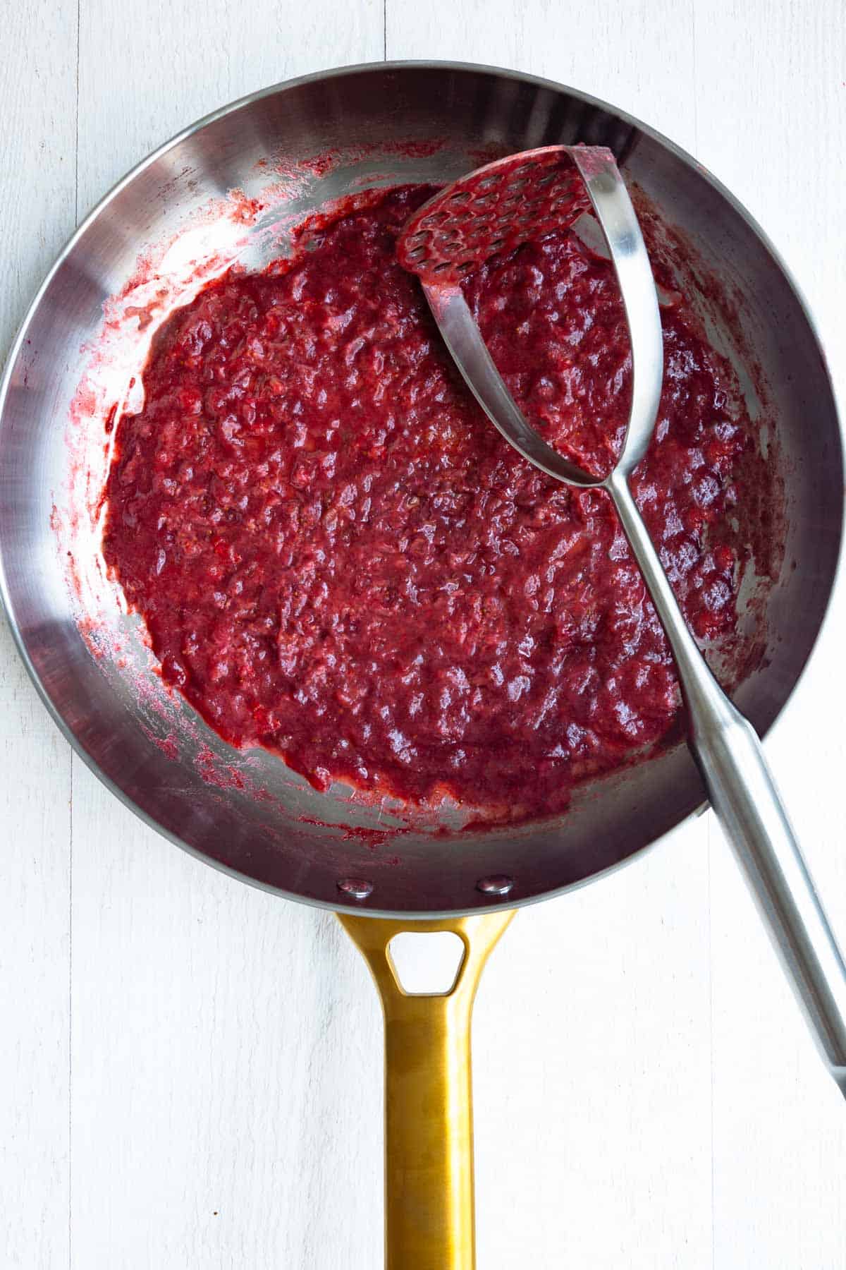 Cooked and mashed strawberries and dates in a stainless steel skillet.