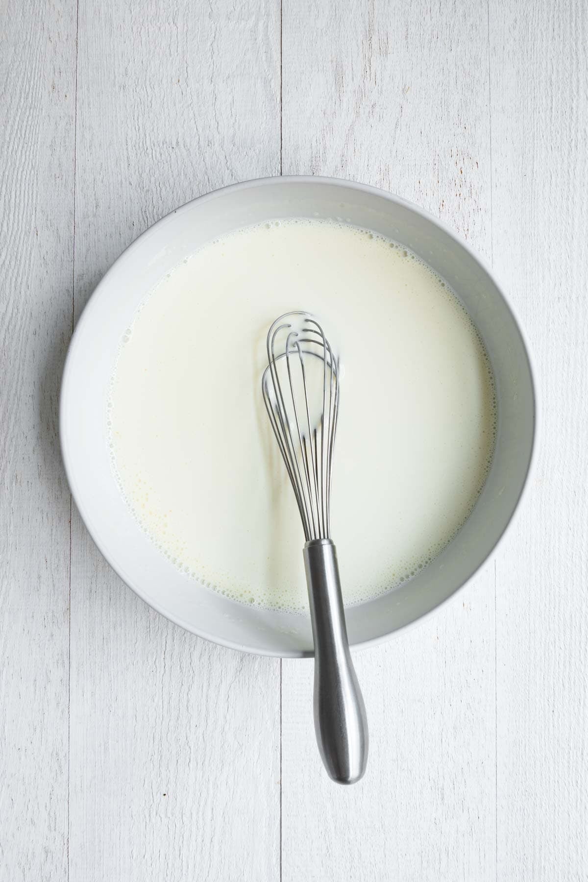 Nondairy milk whisked into Greek yogurt ina. white bowl with a whisk.