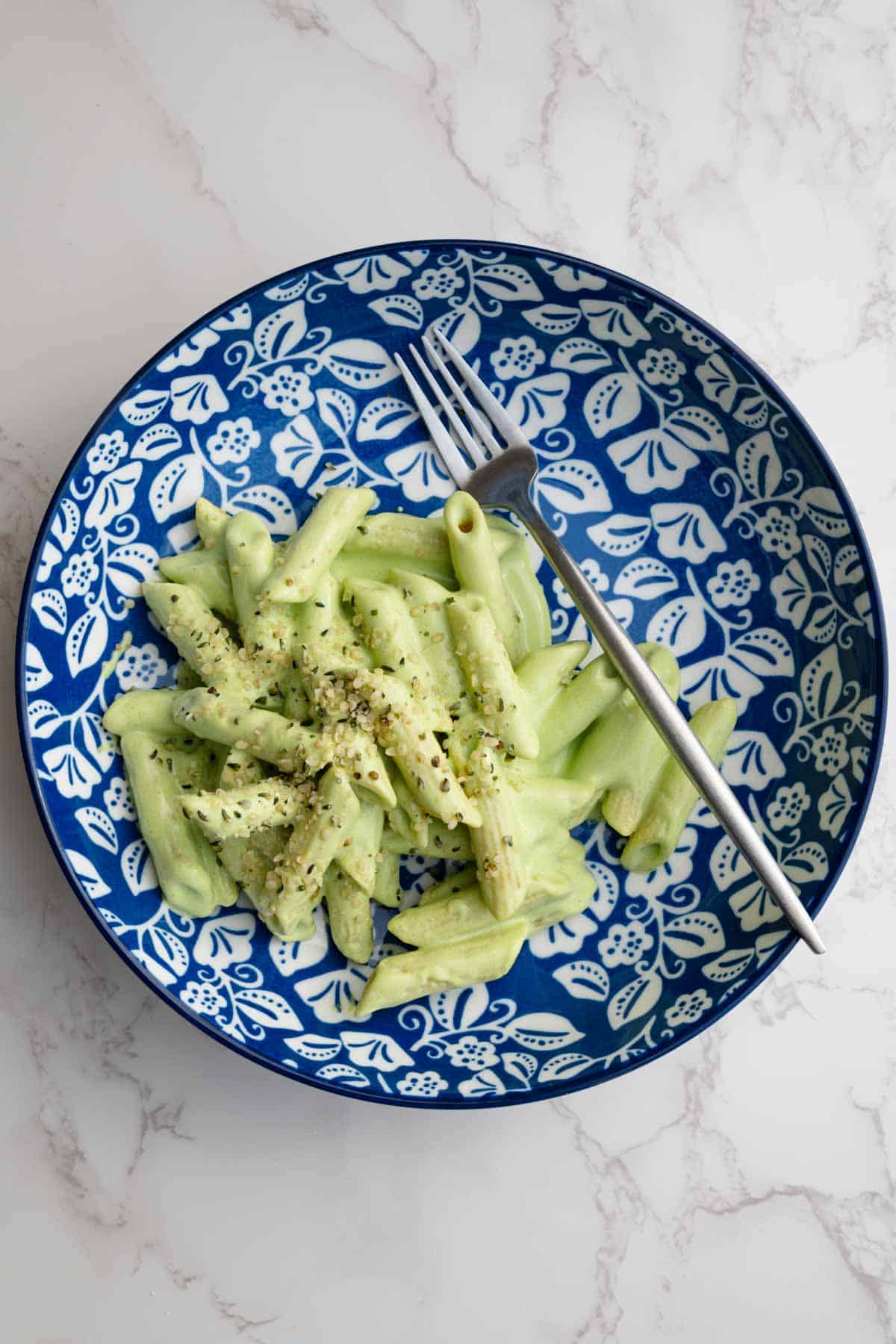 Pasta with green sauce topped with hemp hearts in a bowl with a fork.