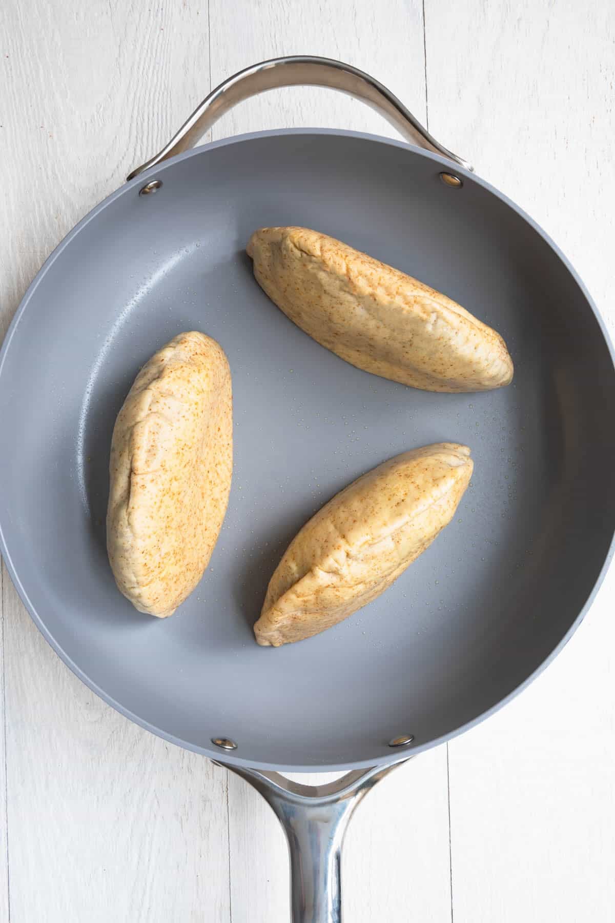 Three stuffed pitas browning in a skillet.