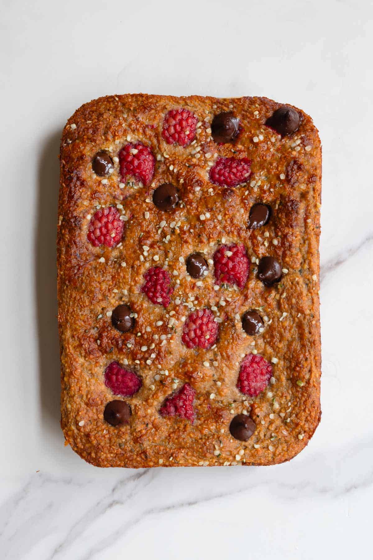 Healthy high-protein banana loaf with yogurt topped with raspberries and dark chocolate on a white plate.