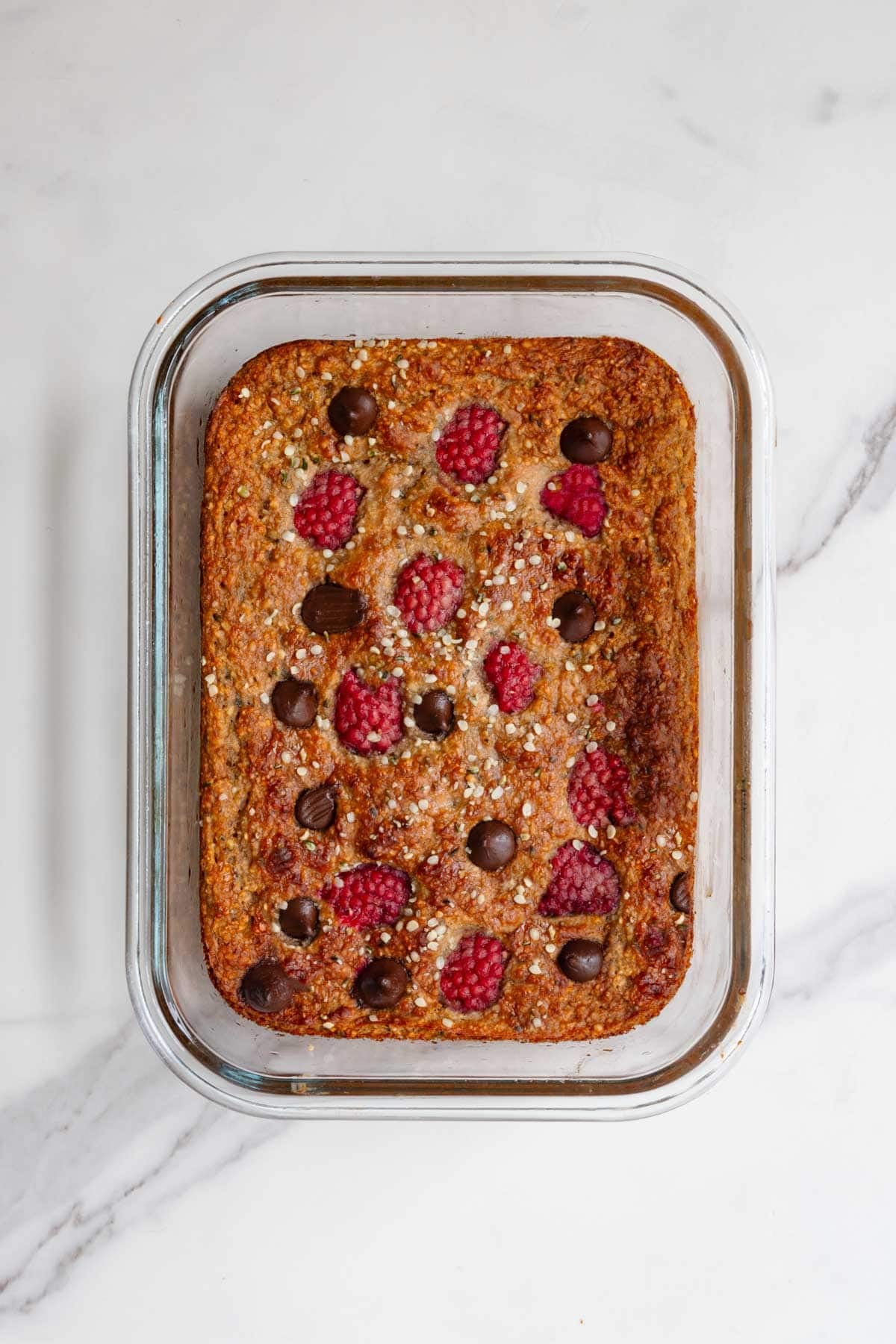 Healthy high-protein banana loaf with yogurt topped with raspberries and dark chocolate in a glass baking dish.