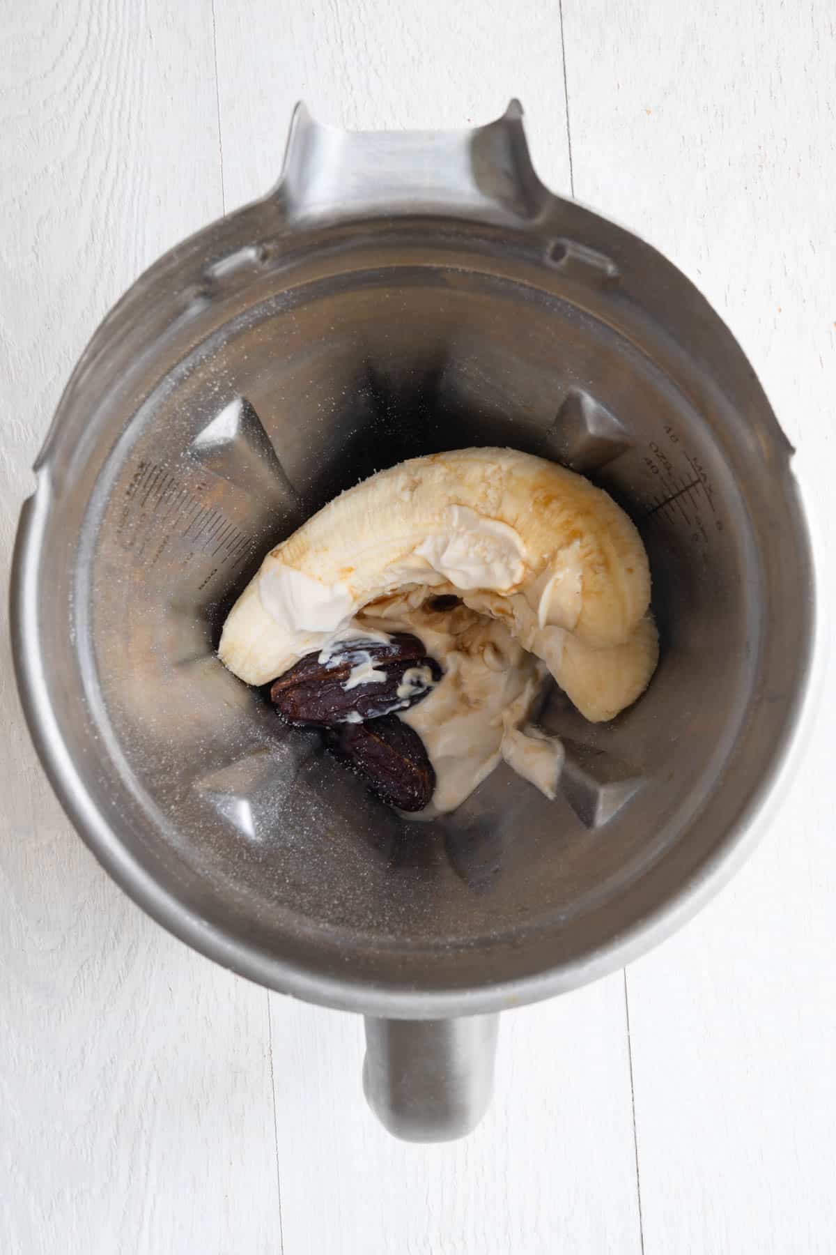 Banana, dates, yogurt, and vanilla in the canister of a blender.