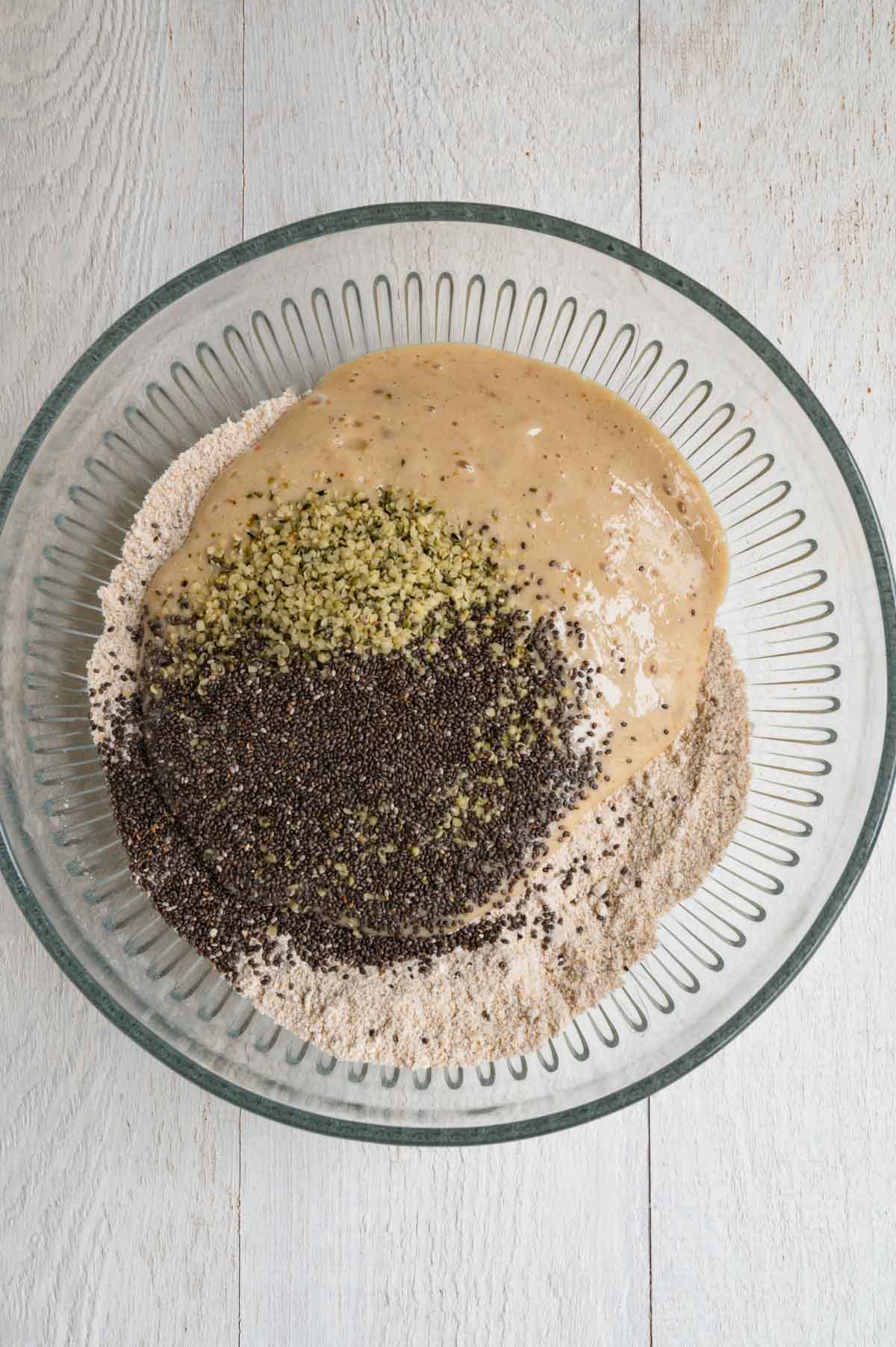 Oat flour, baking soda, baking powder, cinnamon, chia seeds, hemp hearts, and blended banana, dates, vanilla, and yogurt, in a mixing bowl.
