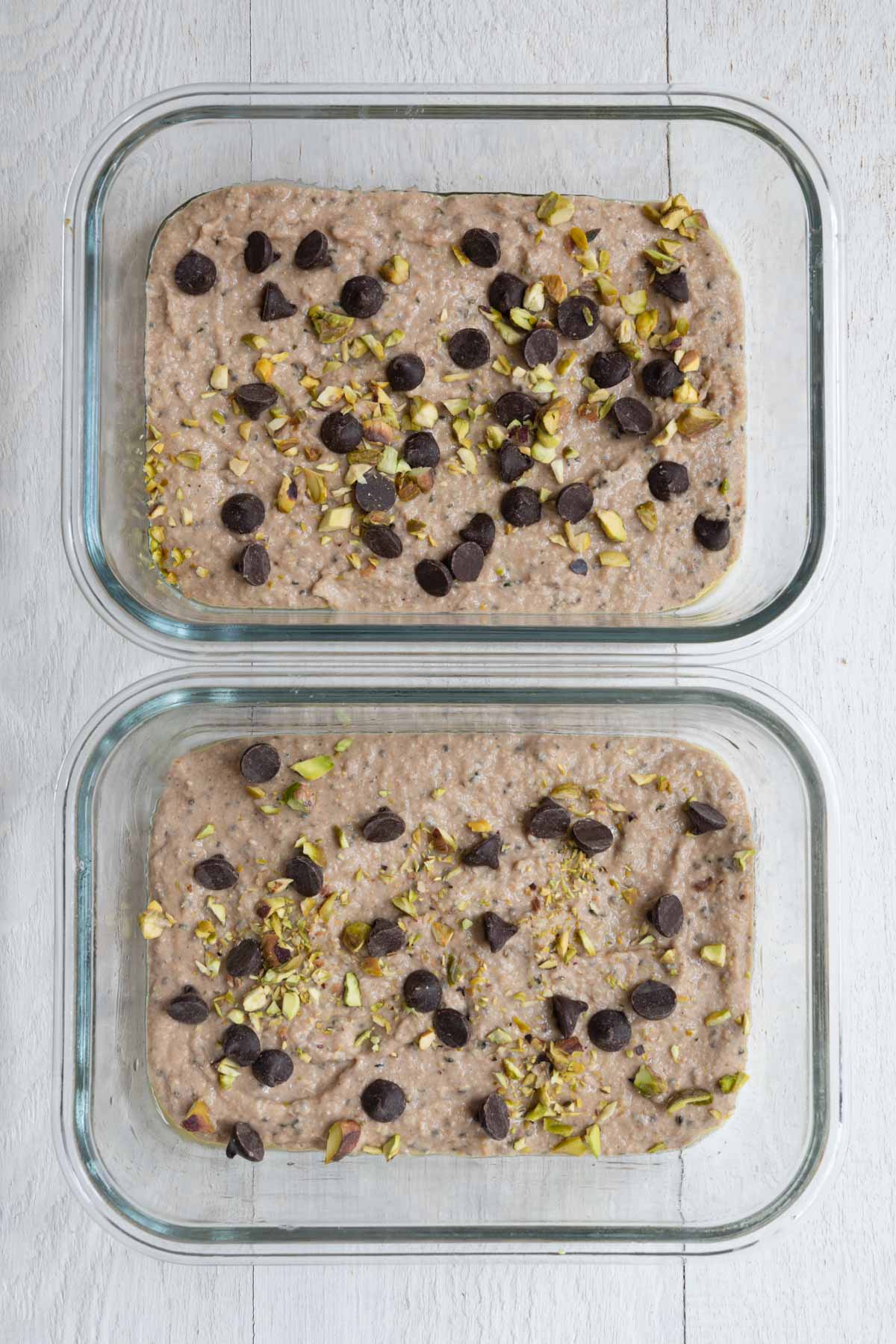 Healthy high-protein banana loaf batter with yogurt in two baking dishes topped with dark chocolate chips and pistachios.