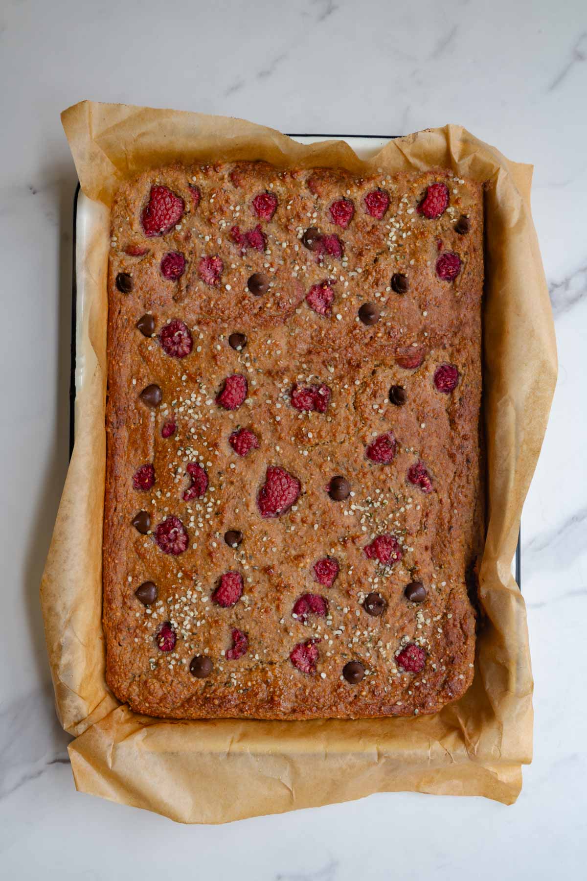 Sheet pan banana bread topped with raspberries and dark chocolate chips.