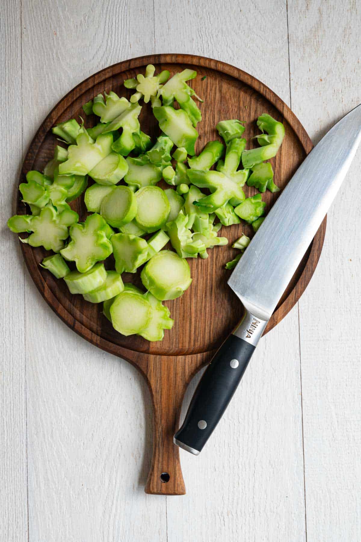Sliced broccoli stems on a wooden cutting board with a cutting knife.