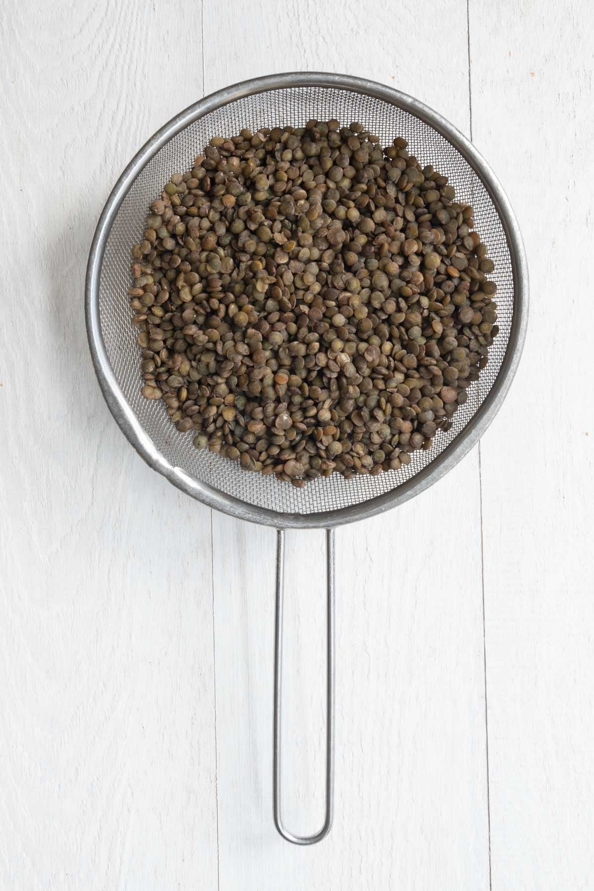 Cooked French lentils draining in a fine mesh sieve.