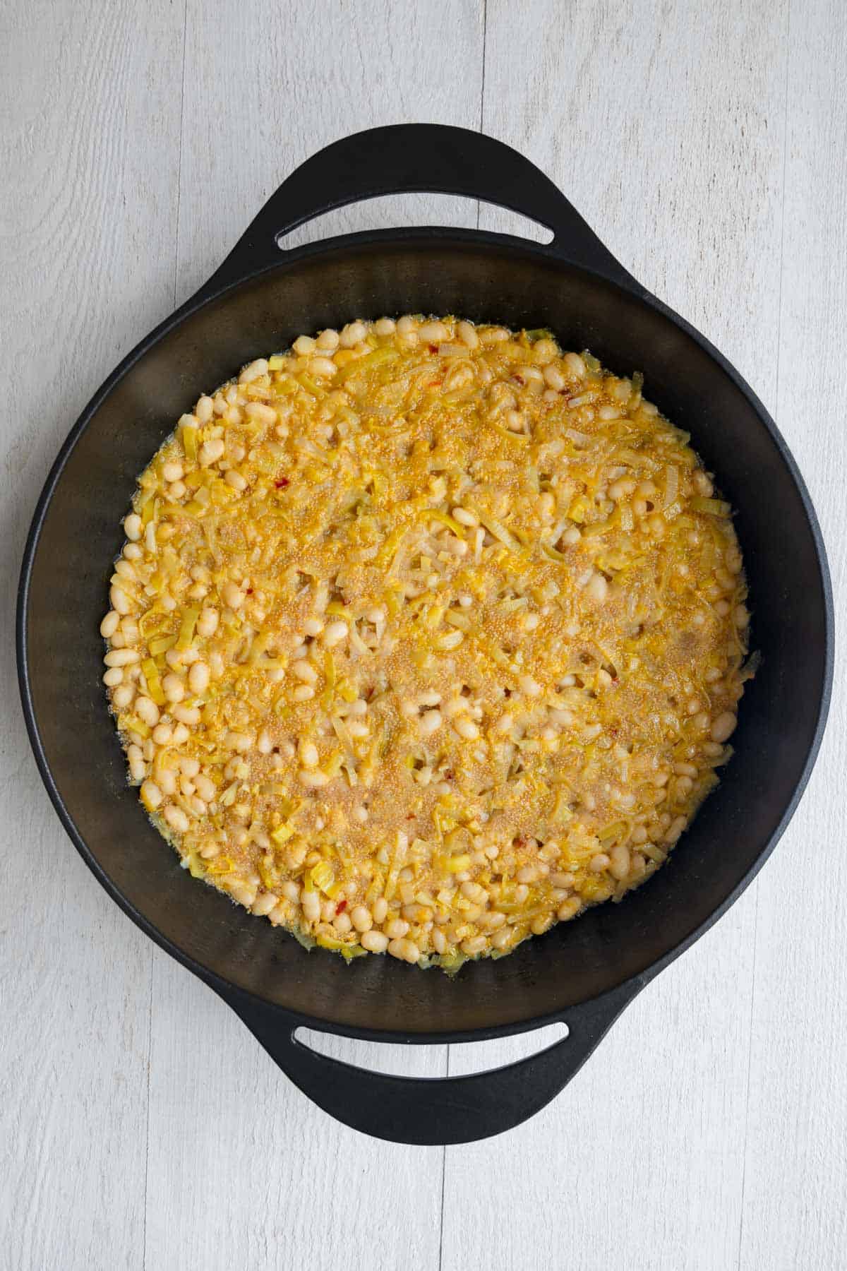 Cooked white beans and amaranth in a large cast-iron skillet with chopped leek.
