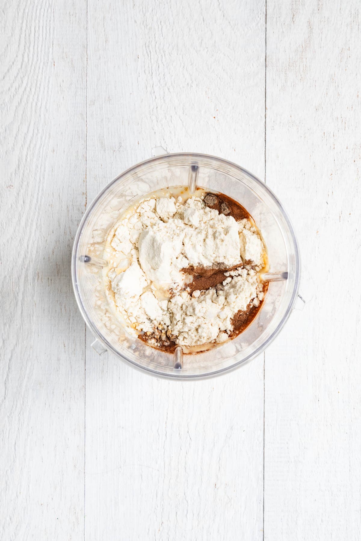Dates, nondairy milk, protein powder, dates, and spices in the canister of a blender.