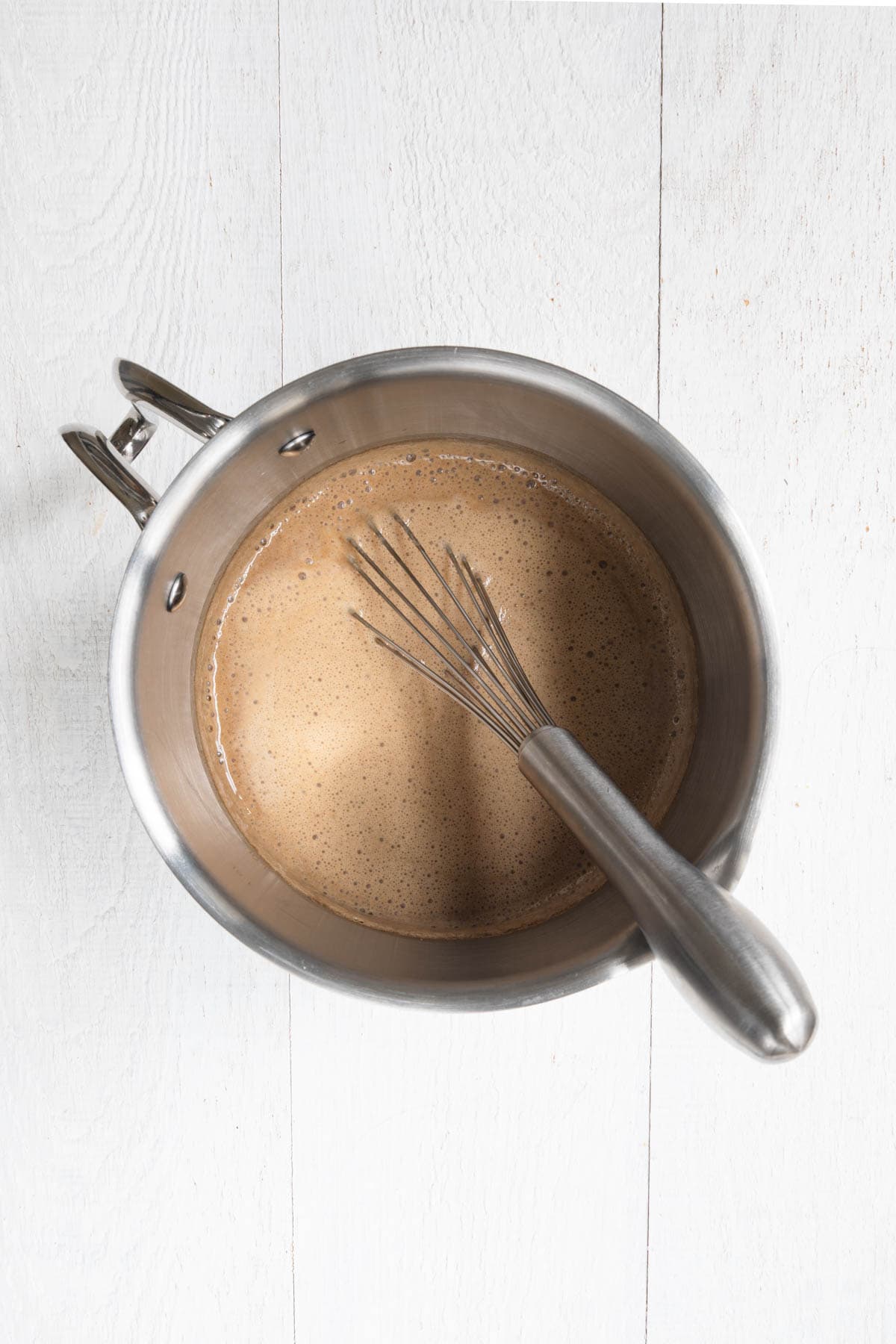 Heated latte in a stainless steel saucepan with a pouring spout.