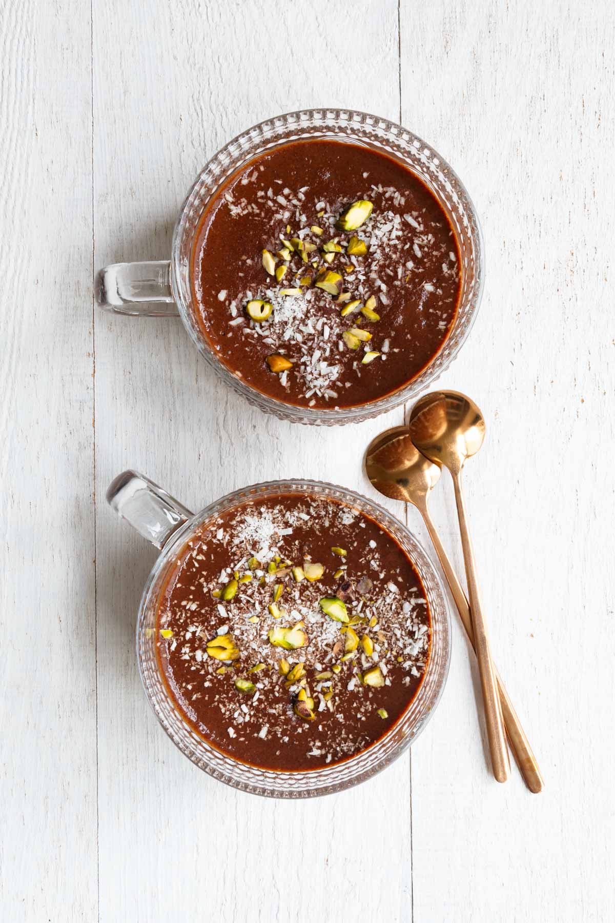 Healthy chocolate pudding topped with pistachios and coconut flakes in two glasses.