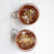 Healthy chocolate pudding topped with pistachios and coconut flakes in two glasses.